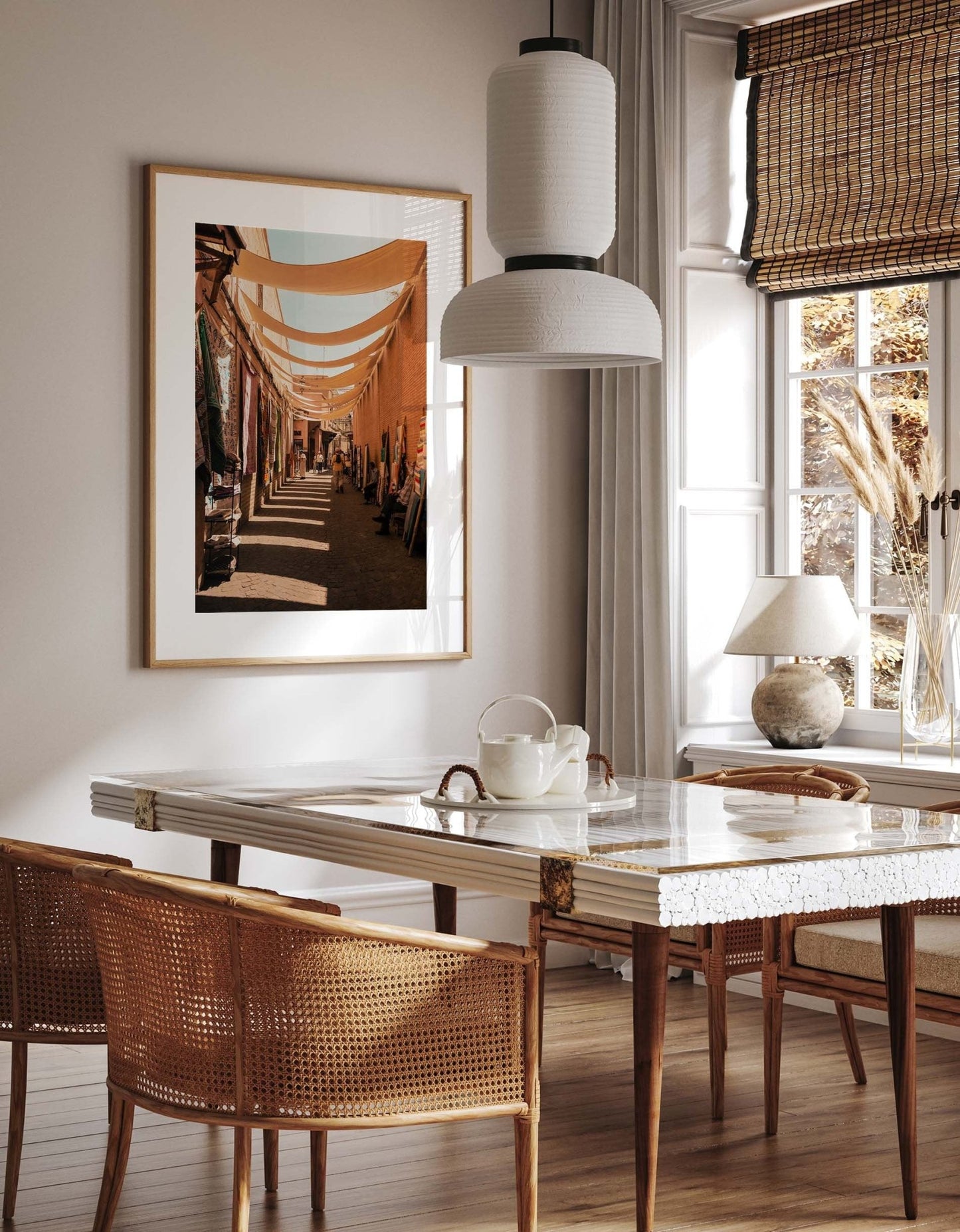 Dining room with a white table, wicker chairs, a hanging light, and Marrakesh Souk I framed artwork on the wall.