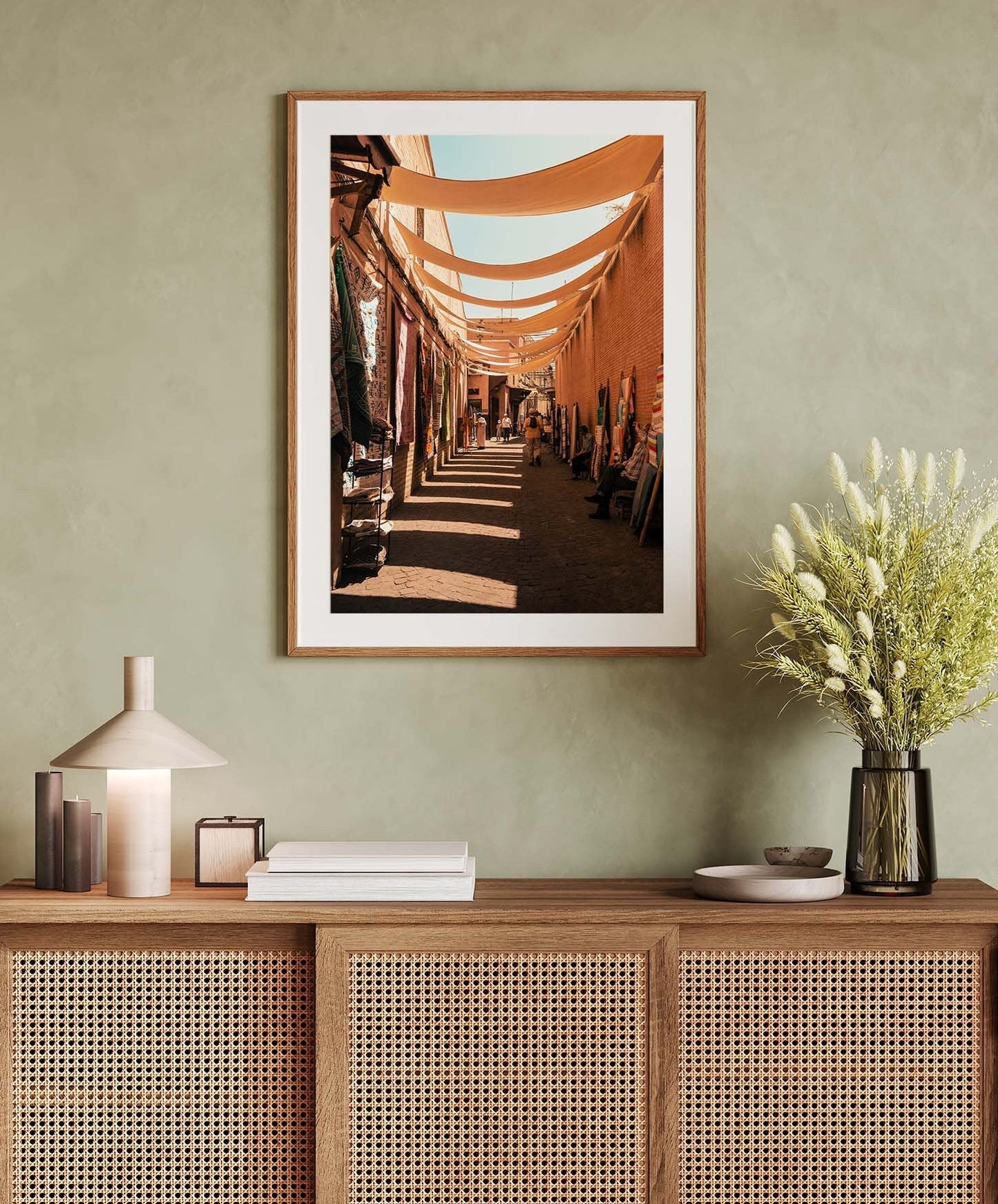 The Marrakesh Souk I photo hangs above a rattan console with a lamp, books, and a vase of flowers.
