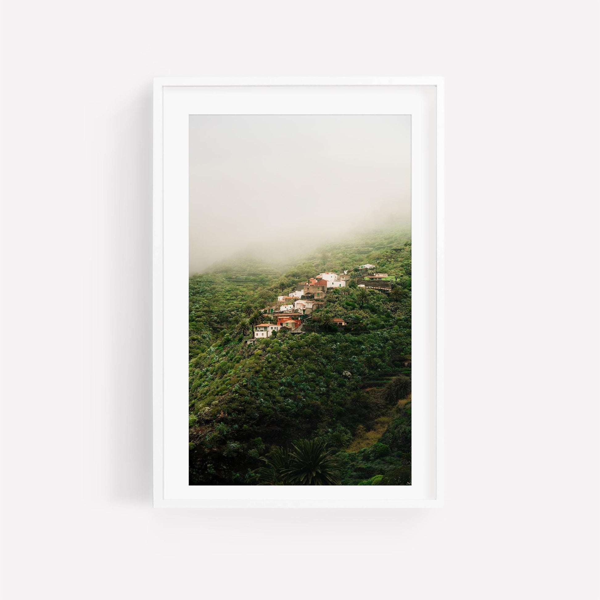 Masca Mist: A cluster of mountainside houses in lush greenery and mist, framed in a white picture frame.