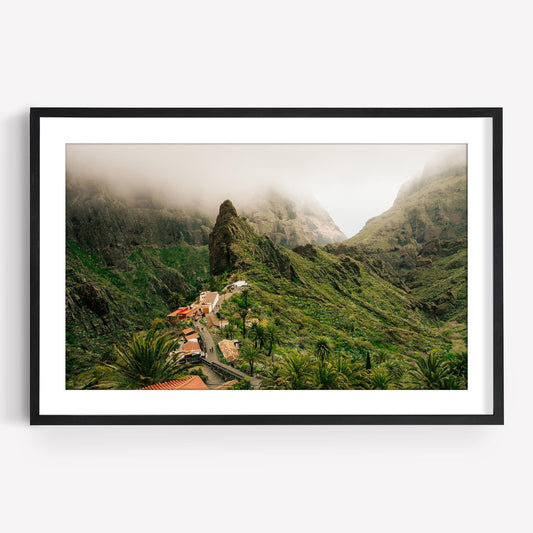 Framed photo of Masca Valley: a lush green mountain landscape with mist and small houses among palm trees.