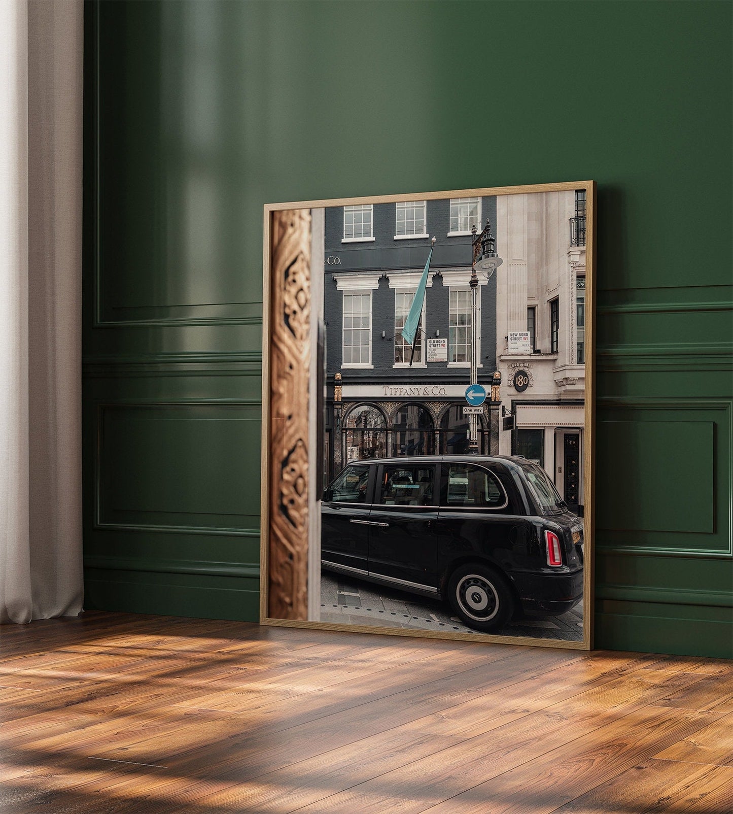 Framed Mayfair Gild photo of a black taxi by a store on a dark green wall over a wooden floor.