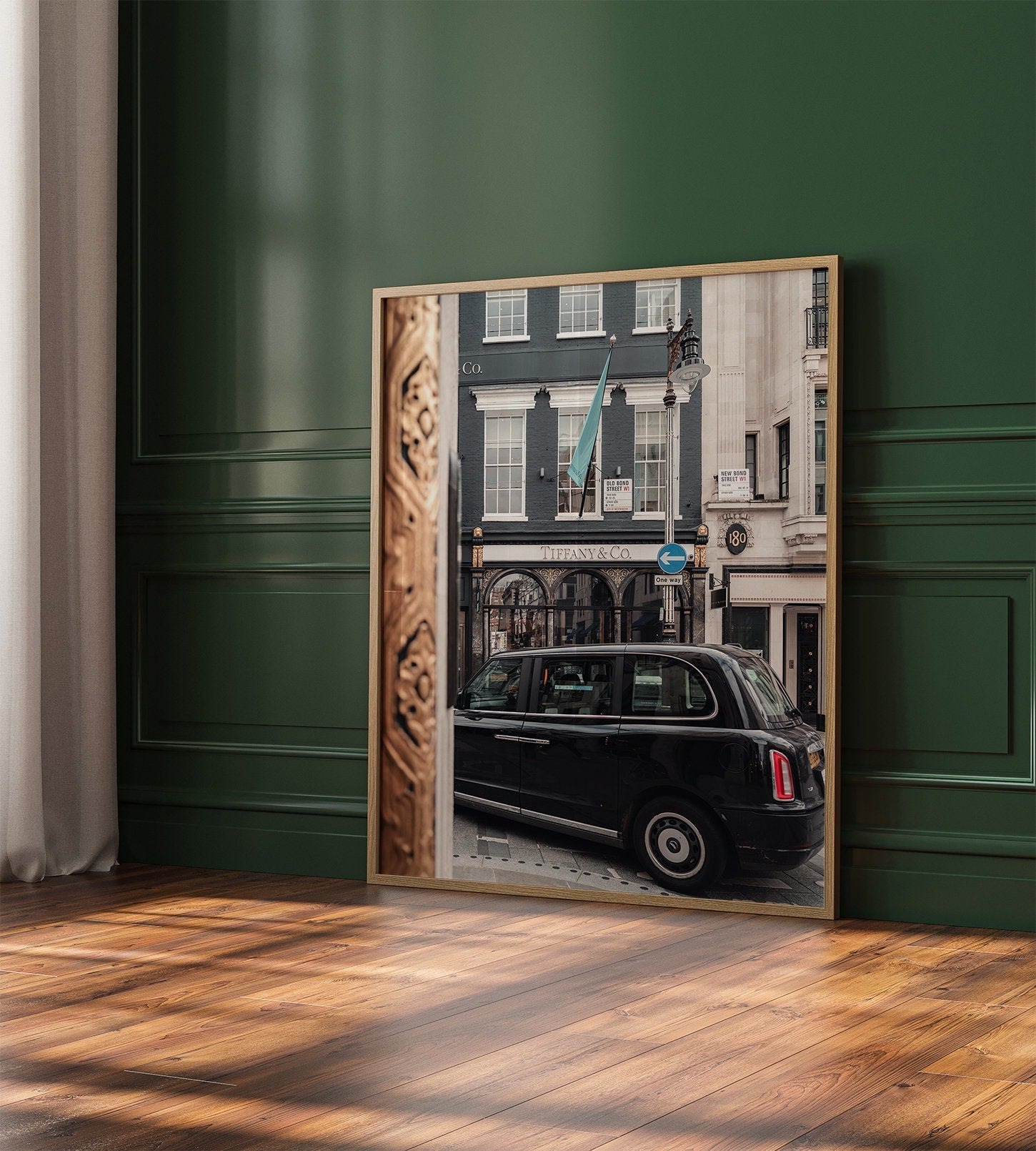 Framed Mayfair Gild photo of a black taxi by a store on a dark green wall over a wooden floor.