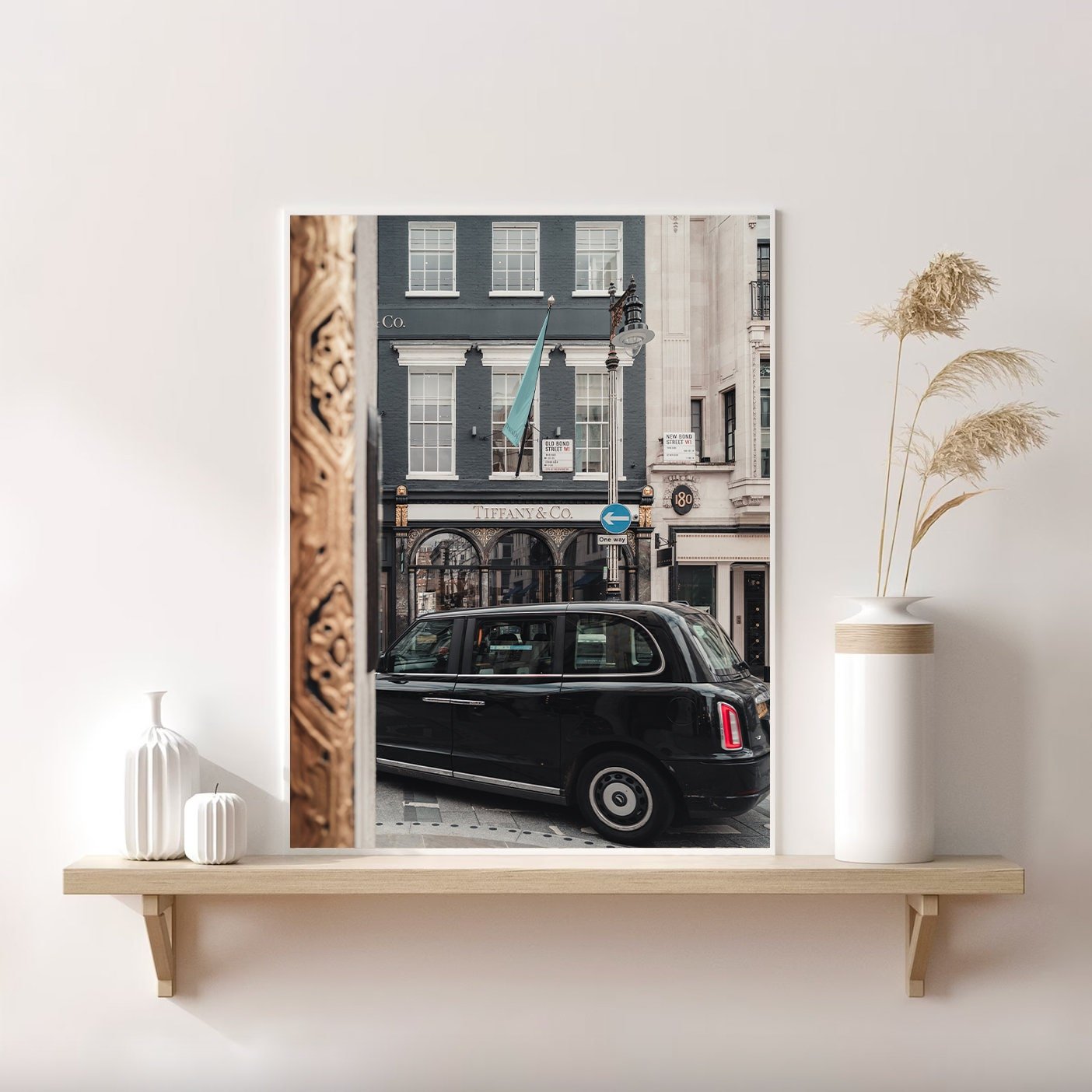 The Mayfair Gild photo of a black taxi and Tiffany & Co. store is displayed on a shelf with vases in a minimalistic room.
