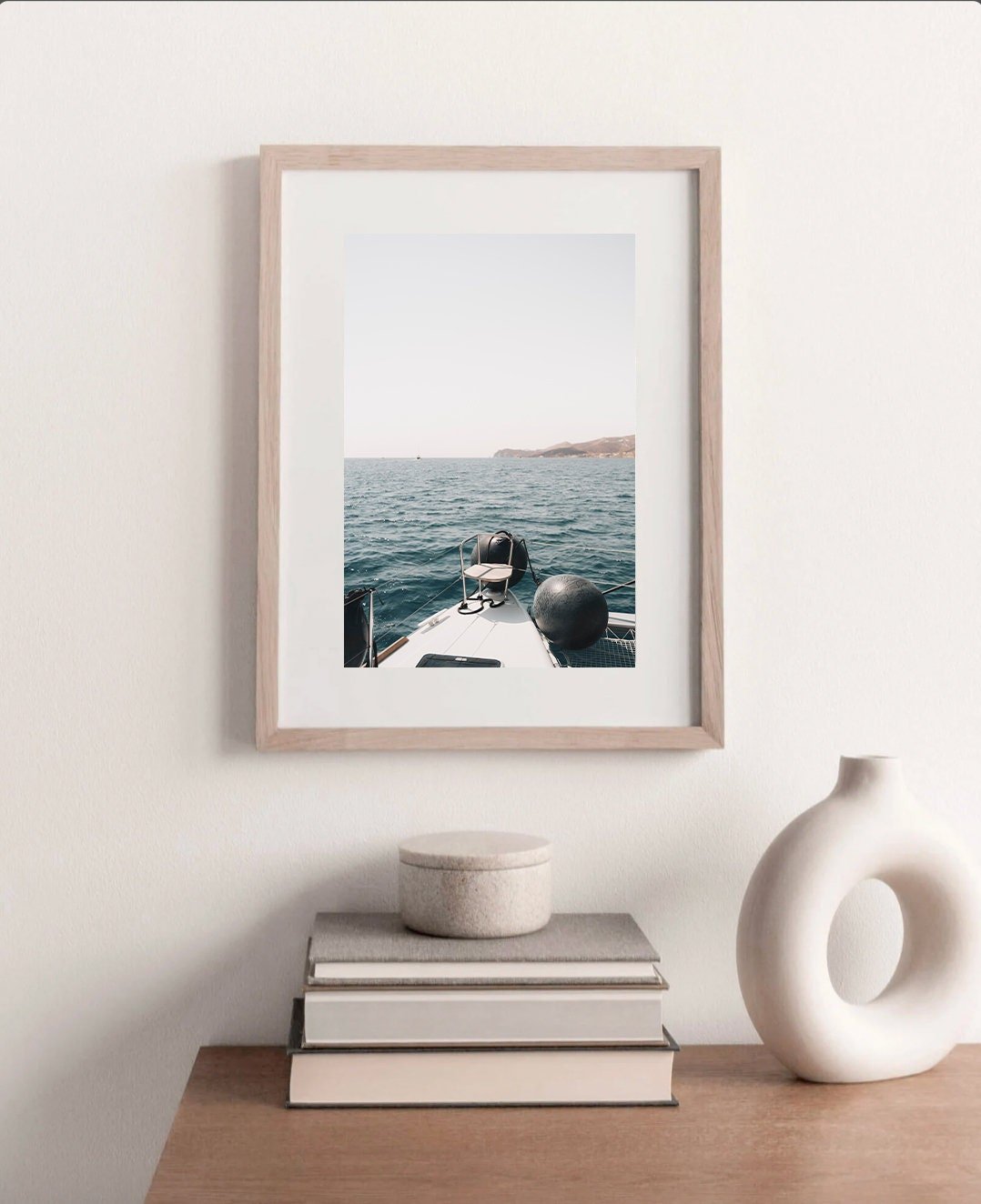 Mediterranean Bliss photo of a boat on calm sea, displayed above a wooden table with decorative items and books.