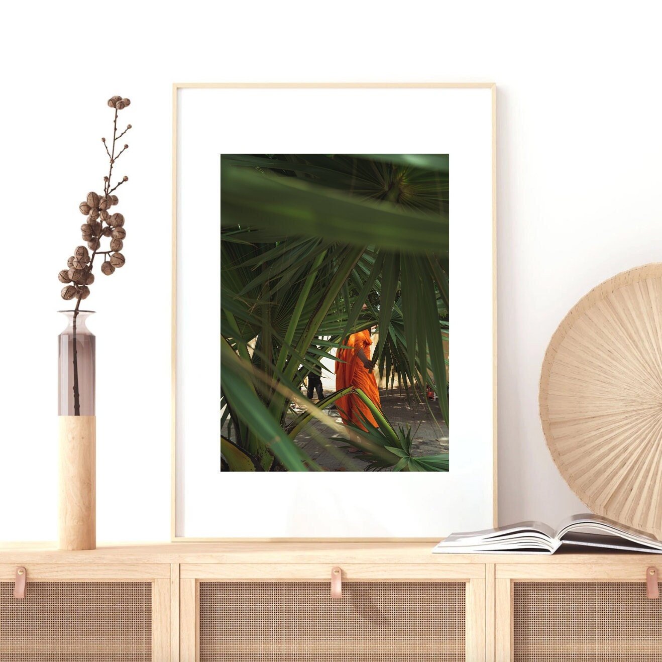 Framed photo Monk of a person in red amidst green leaves, on a wooden shelf with decor items.