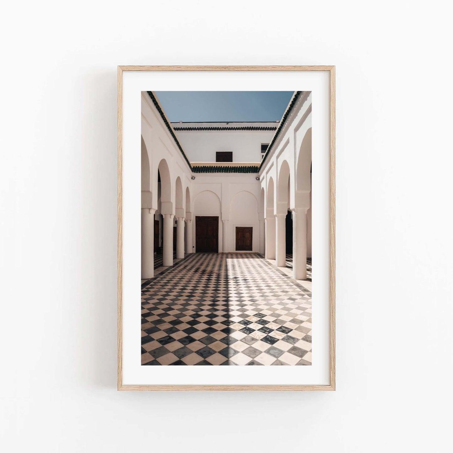 Framed Moroccan Architecture I photo features a sunlit courtyard with arches and a checkered floor against a plain wall.