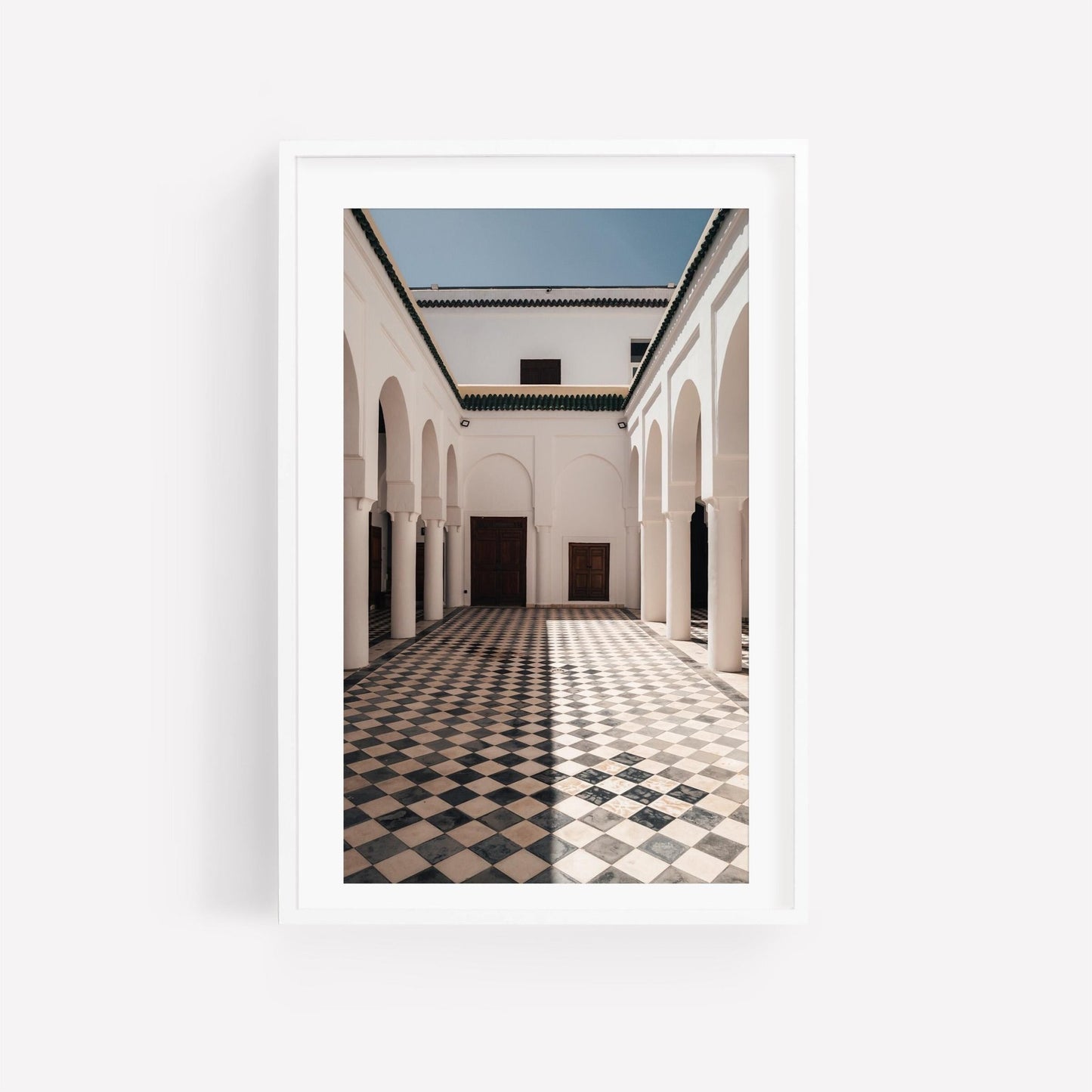 A framed photo titled Moroccan Architecture I featuring a sunlit courtyard with arches and checkered tile floor.