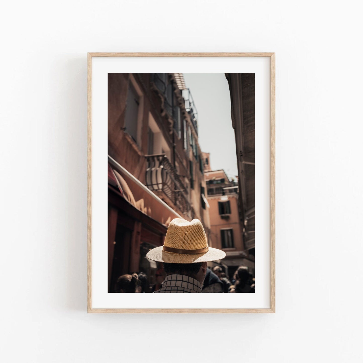Framed Mystery Man photo: a person in a straw hat walking down a narrow street with tall buildings.