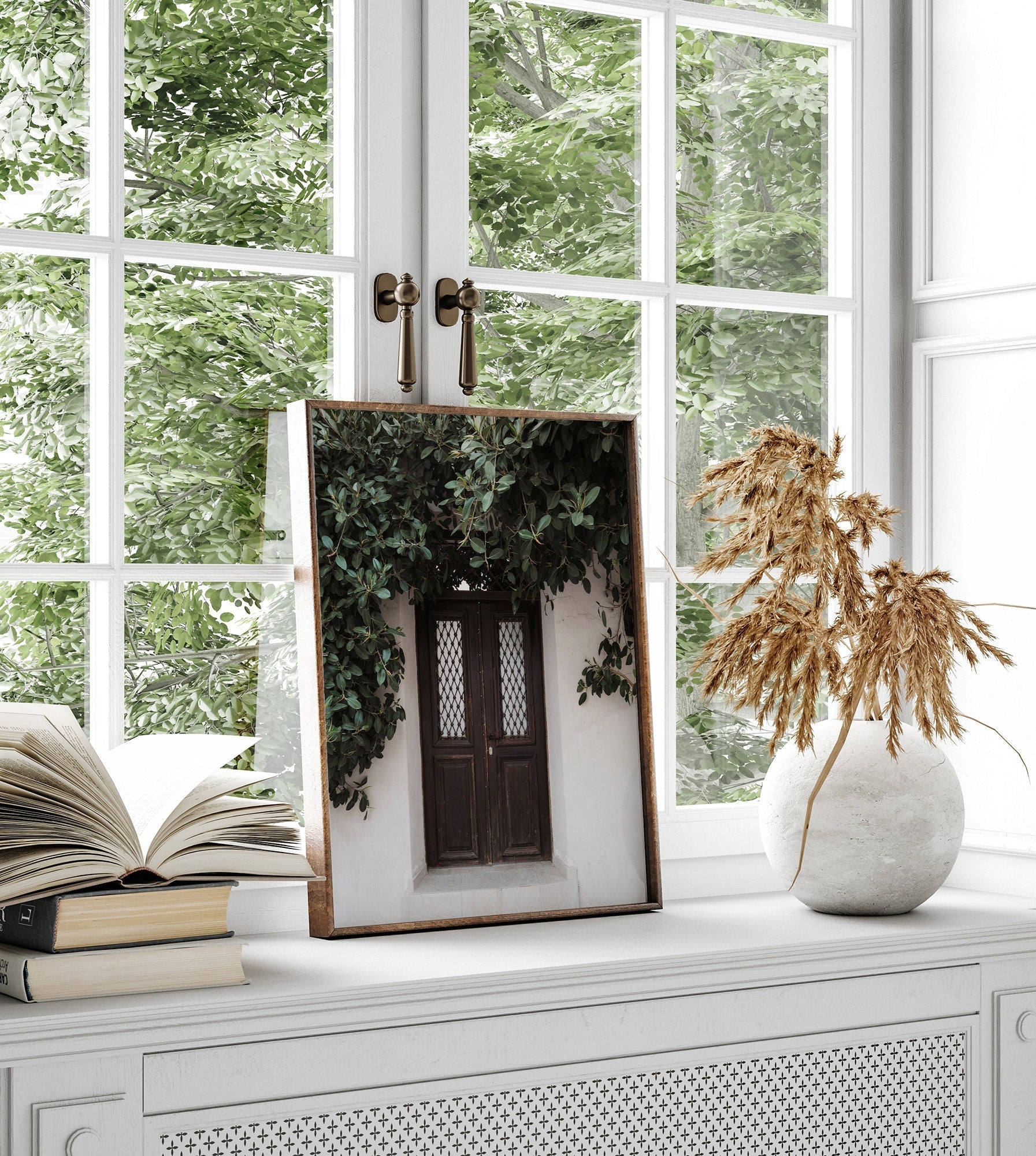 Natures Door window reflect a vine; nearby are books and a vase with dried grass on a white shelf.