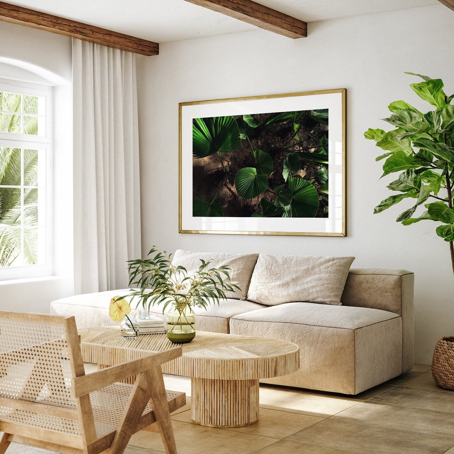 A bright living room features a beige sofa, bamboo coffee table, leafy artwork, large plant, and a side window. Natures Glow.