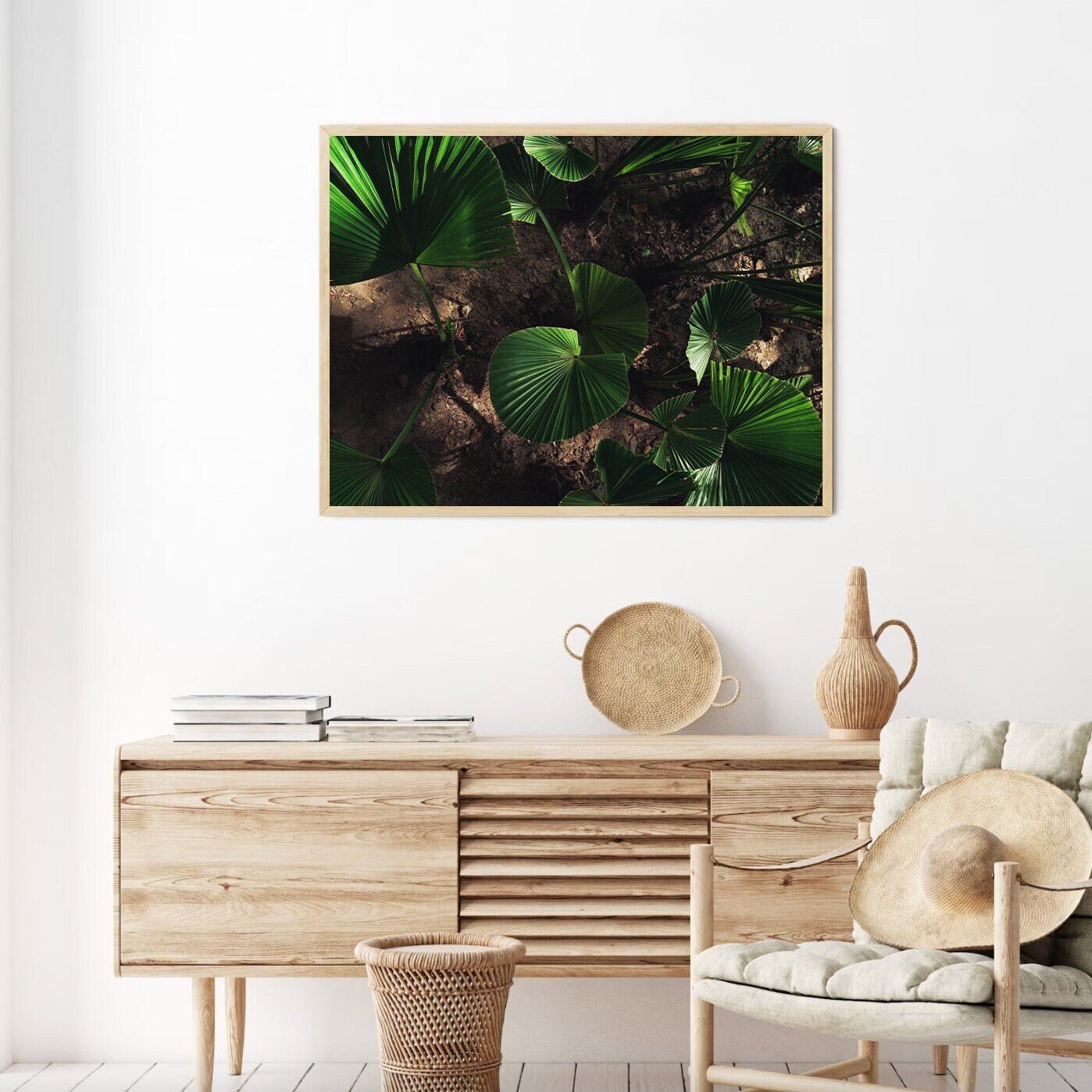 Minimalist living room with Natures Glow wooden console, wicker chair, and framed leaf art on a white wall.