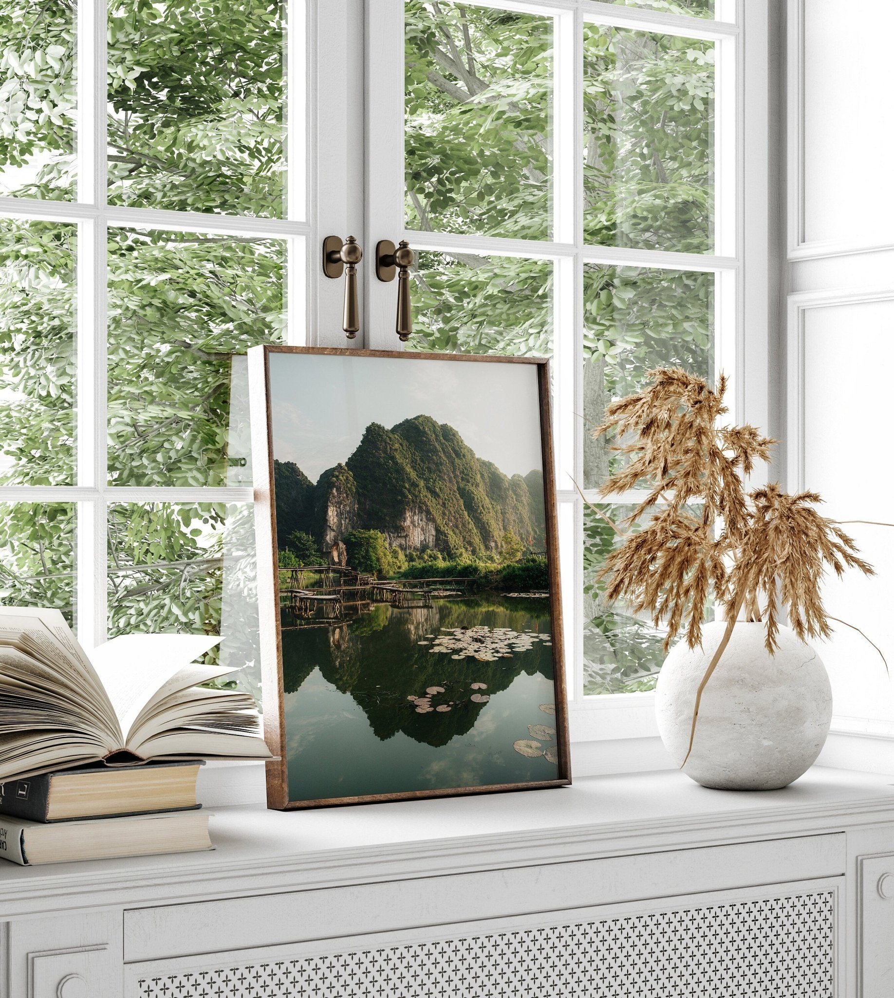 The framed Natures Symmetry photo is beside books and a vase on a white cabinet beneath a window.