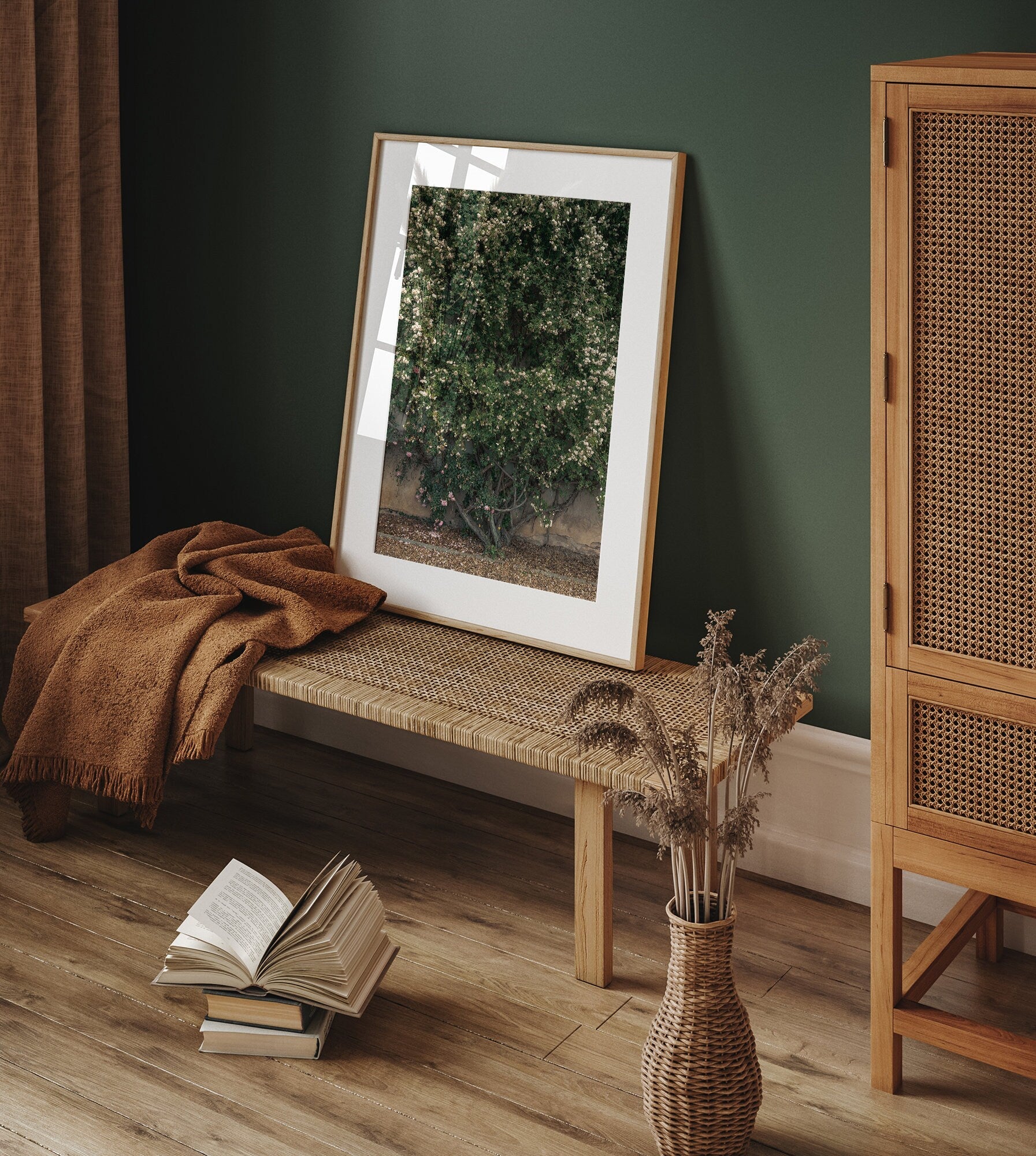 Natures Wall framed photo rests on a woven bench, with a blanket and book in a cozy, green-toned room.