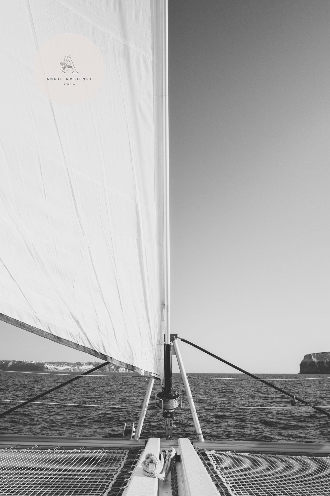 Black and white photo from Nautical Elegance Black and White - Set of 3: sailboat at sea with cliffs in the distance.