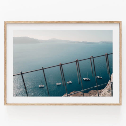 Framed Nautical Formation photo features a serene ocean view with sailboats through a fence under a clear blue sky.