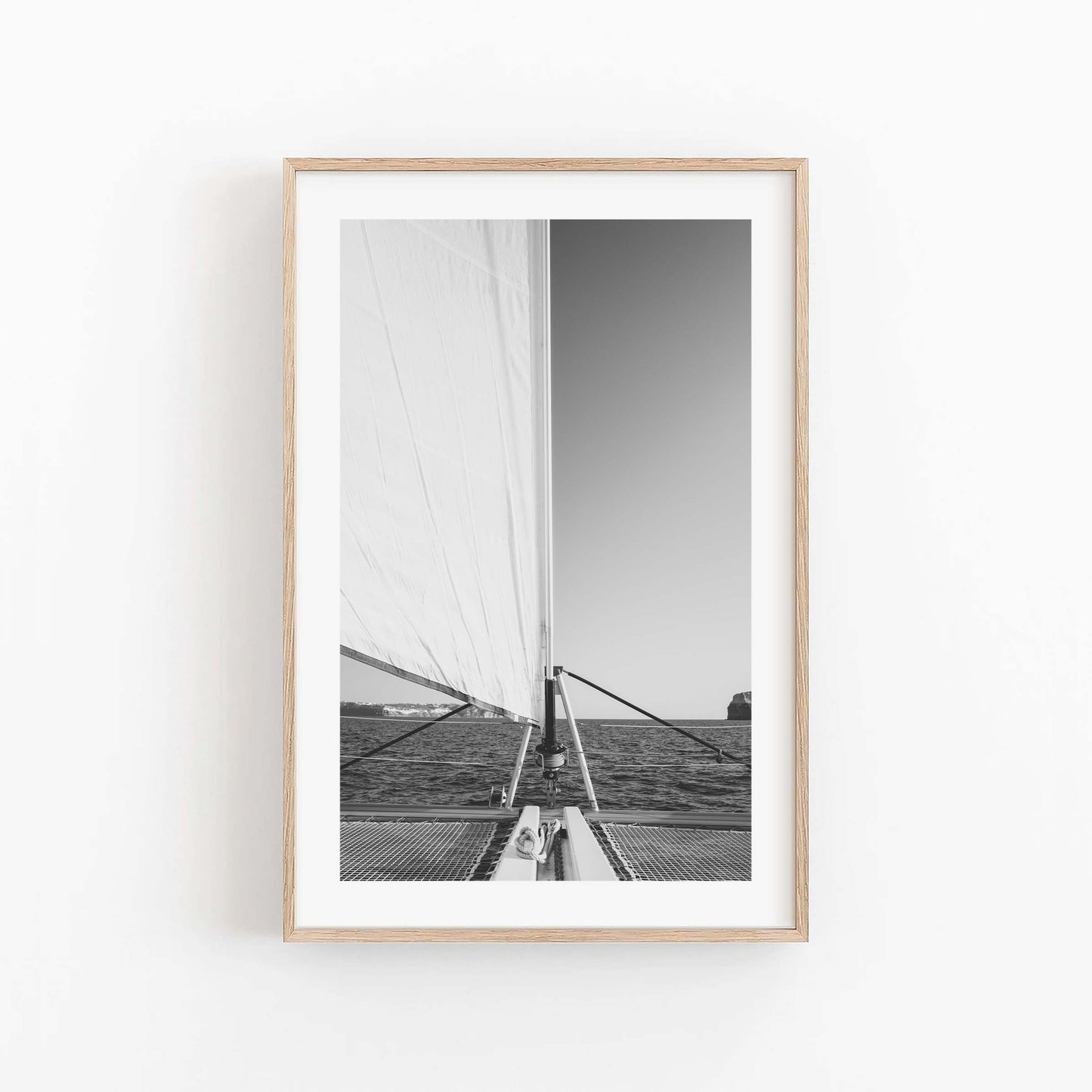 Black and white photo of a sailboat on the water, framed in light wood. Product: Nautical Harmony Black and White.