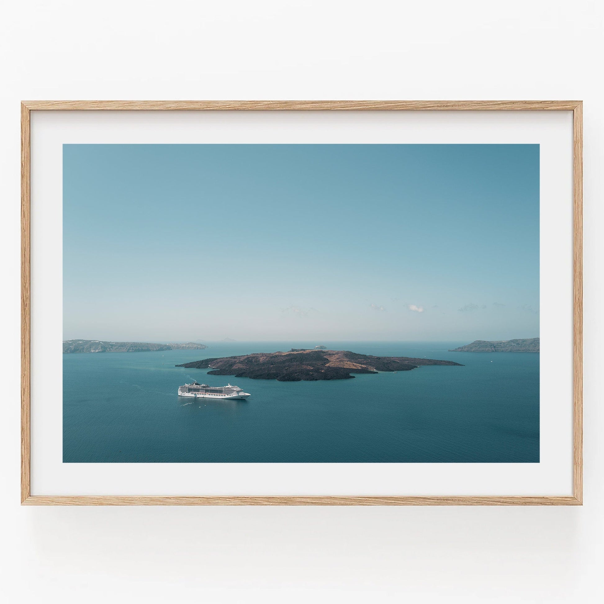 Aerial view of Nea Kameni cruise ship near island in calm blue waters, in a light wooden frame against a white background.