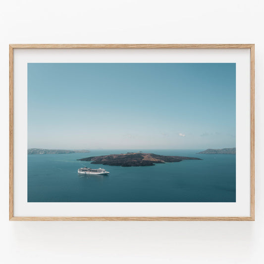 Aerial view of Nea Kameni cruise ship near island in calm blue waters, in a light wooden frame against a white background.