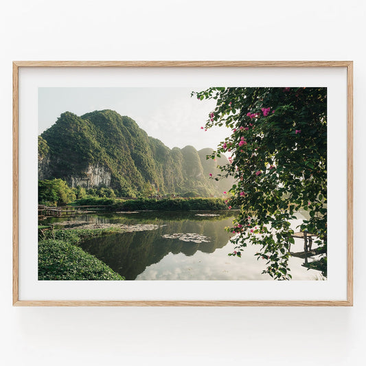 Framed photo titled Ninh Binh Serenity, featuring scenic lake with green hills and flowering plants.