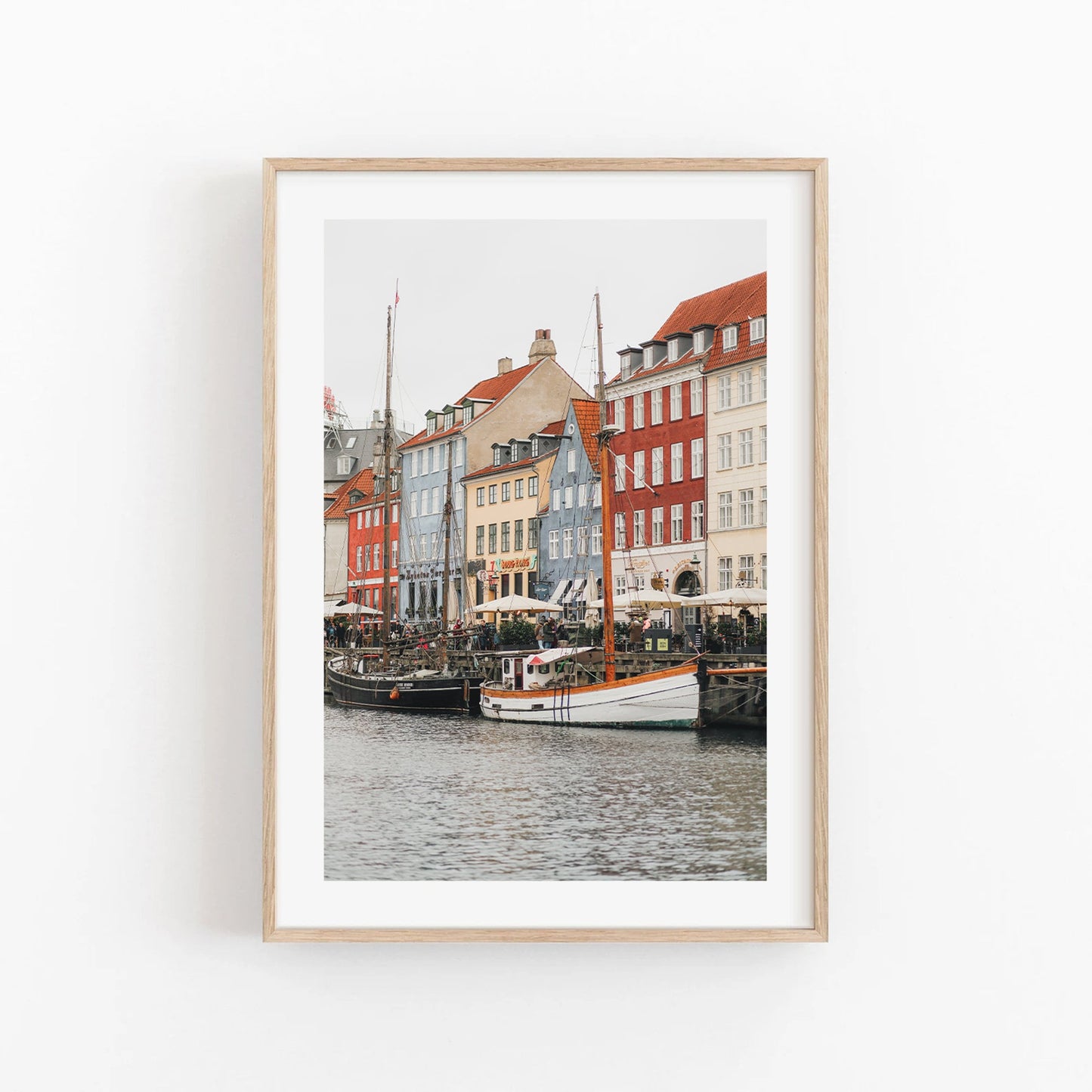 Framed photo of colorful buildings and boats, likely Nyhavn in Copenhagen, against a white background. Product: Nyhavn Canal.
