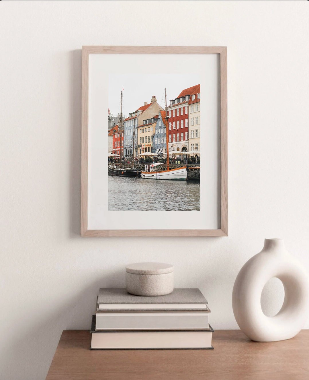 Framed Nyhavn Canal photo above a table with books and ceramic decor.