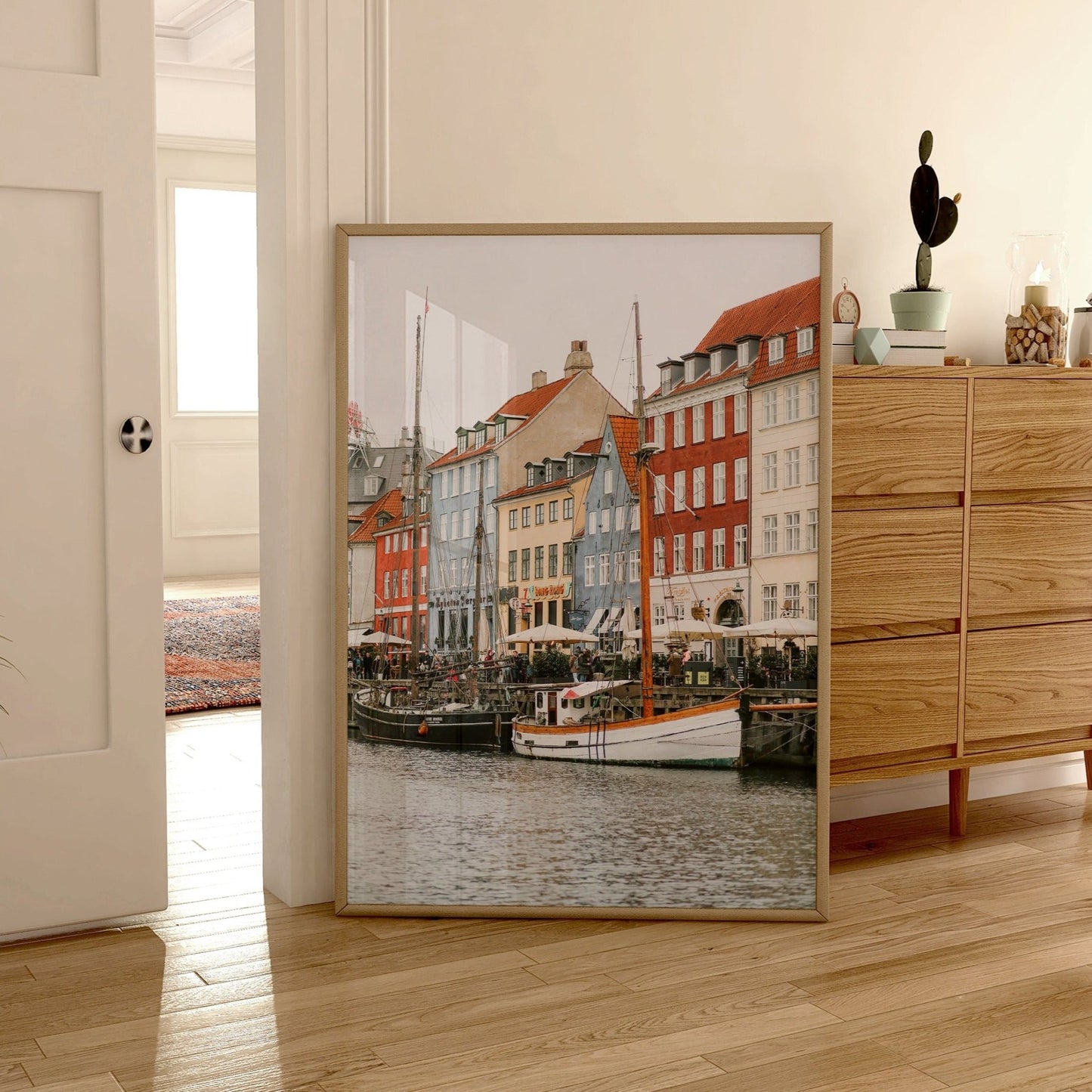 Nyhavn Canal framed photo of vibrant buildings and boats in a harbor, leaning against a modern rooms wooden furniture.
