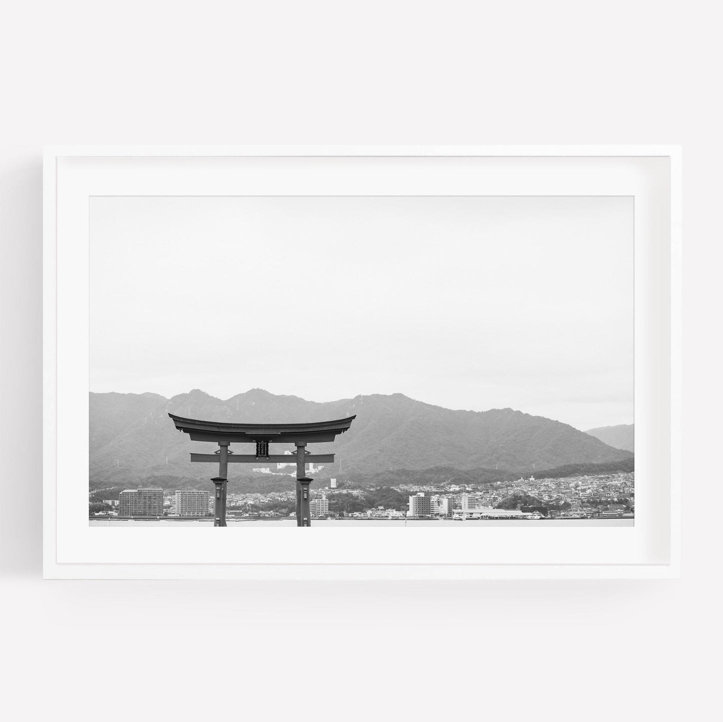 Black and white photo of the O-Torii Gate in water, with mountains and a cityscape in the background.