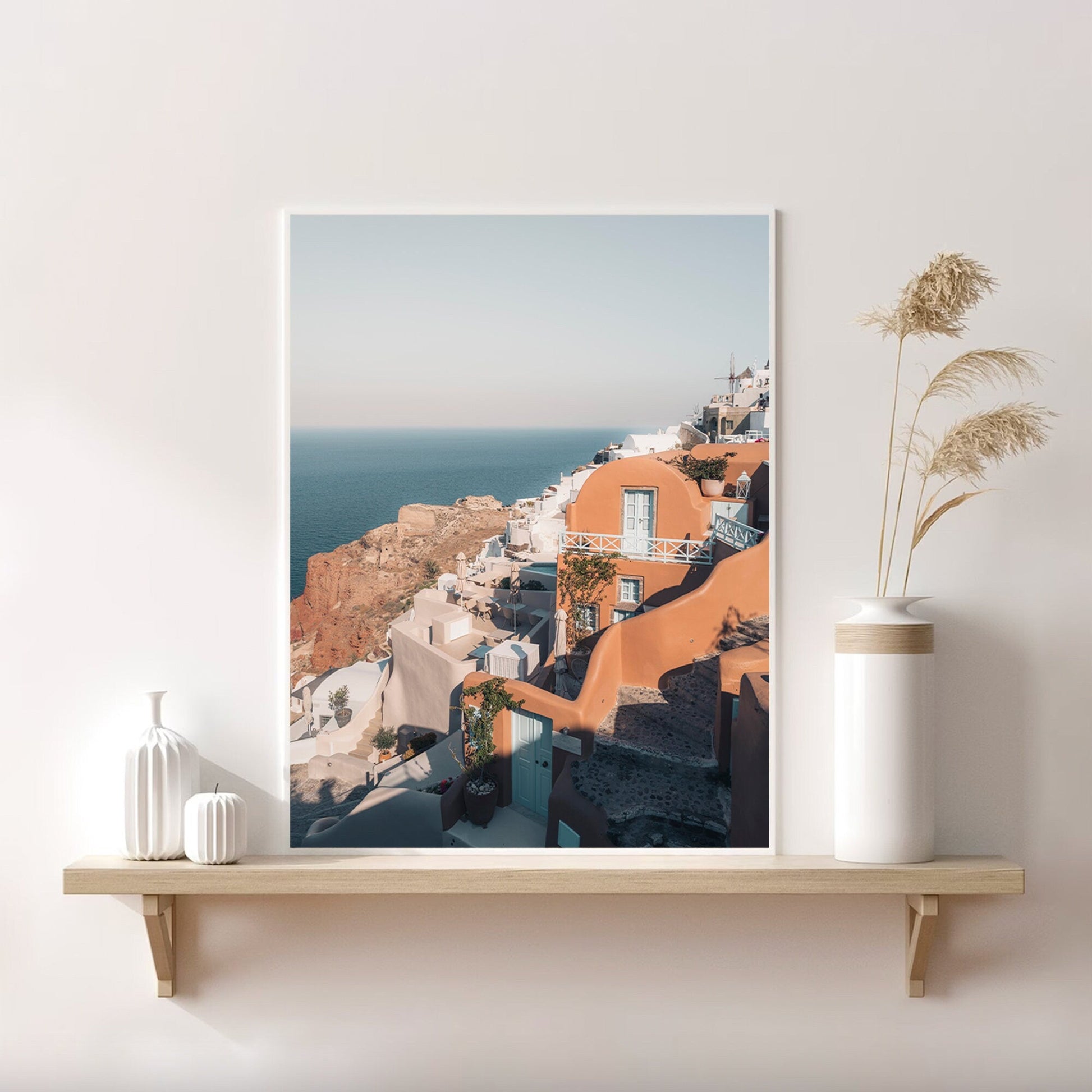 Framed Oia photo on a shelf with decorative white vases and dried pampas grass.