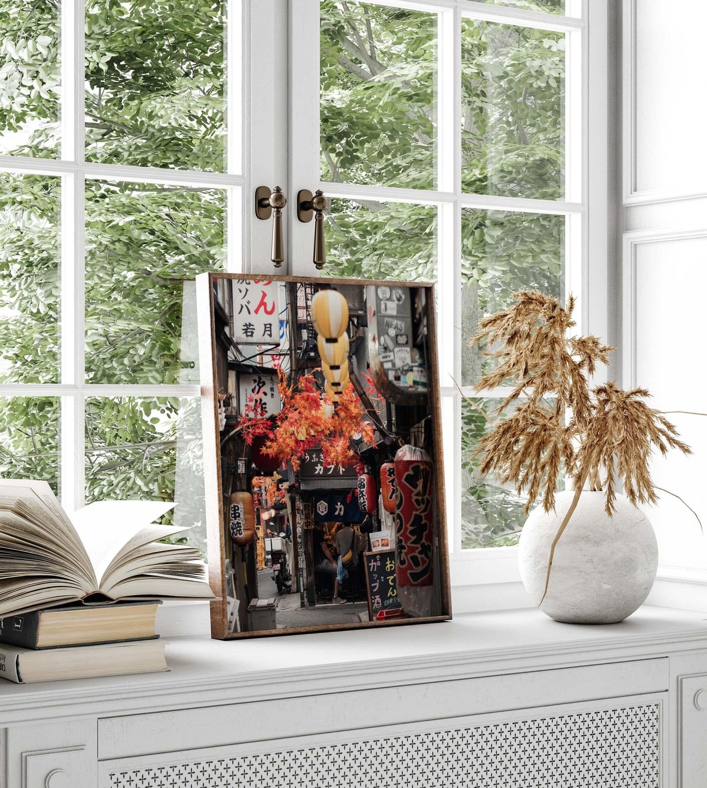 The Omoide Yokocho art print features an urban scene, elegantly displayed on a white shelf with books and a vase of dried flowers.