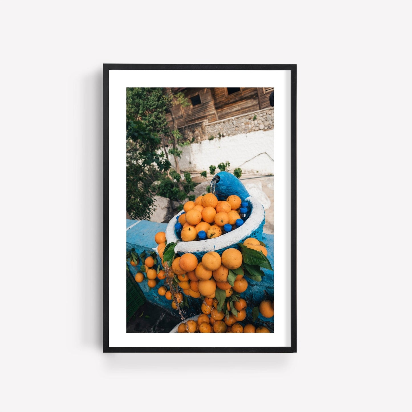 A Orange Fountain framed photo features a basket of ripe oranges in an outdoor setting.