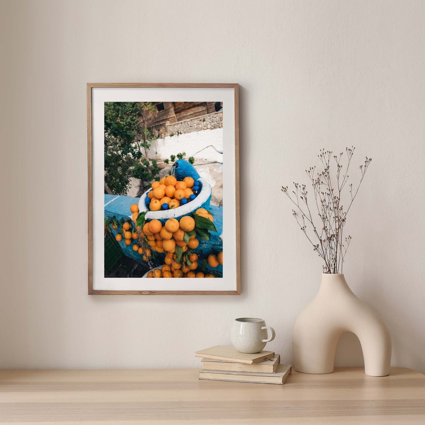 Orange Fountain framed photo on wall above shelf with vase and cup.