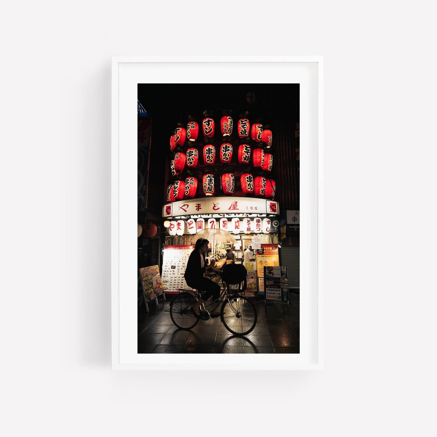 The Osaka Lantern Biker features a silhouette of a person cycling past a brightly lit shop adorned with red lanterns at night.