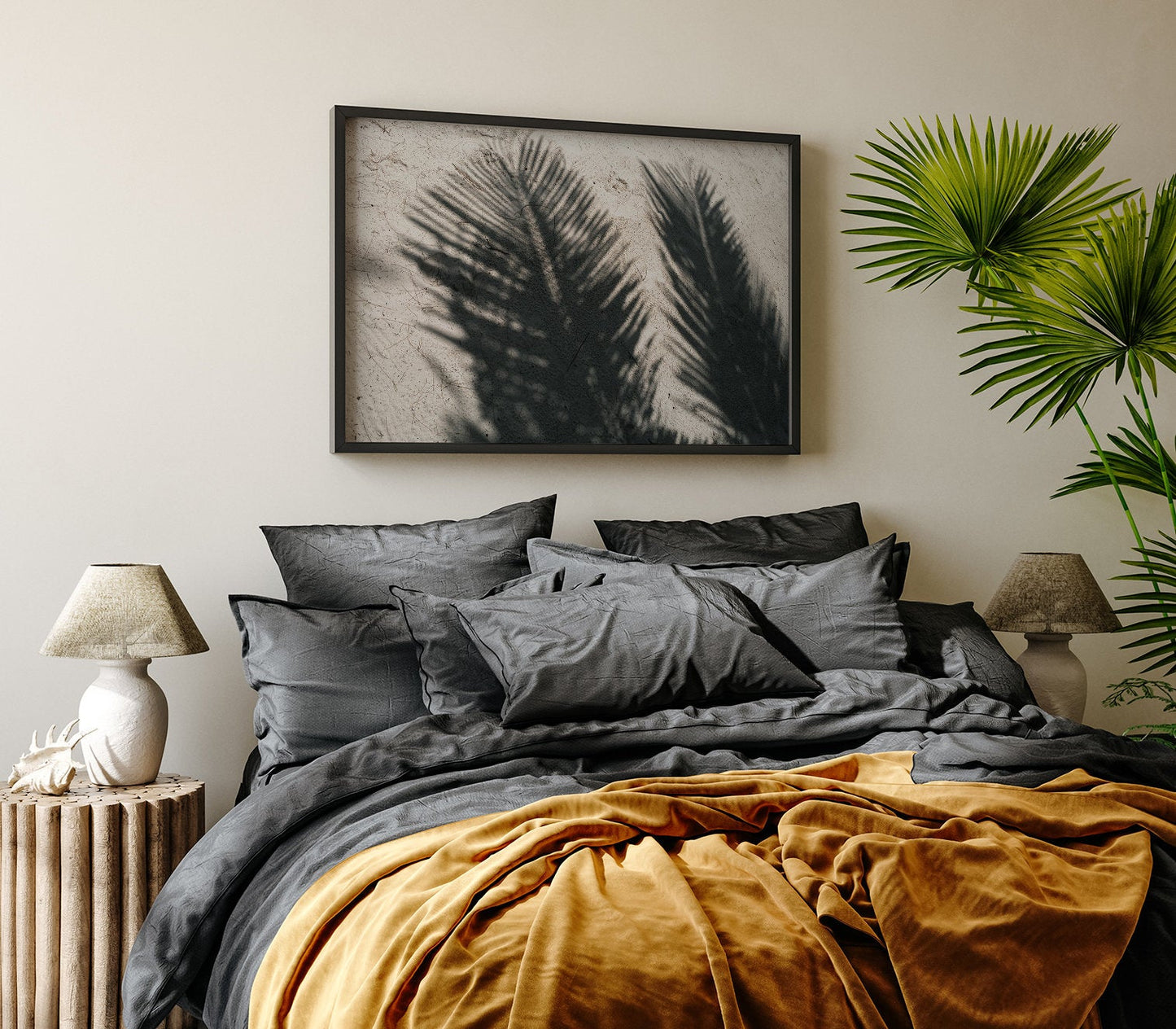 A cozy bedroom with a large bed, dark pillows, and mustard blanket. Palm Shade art and plants add a tropical vibe.