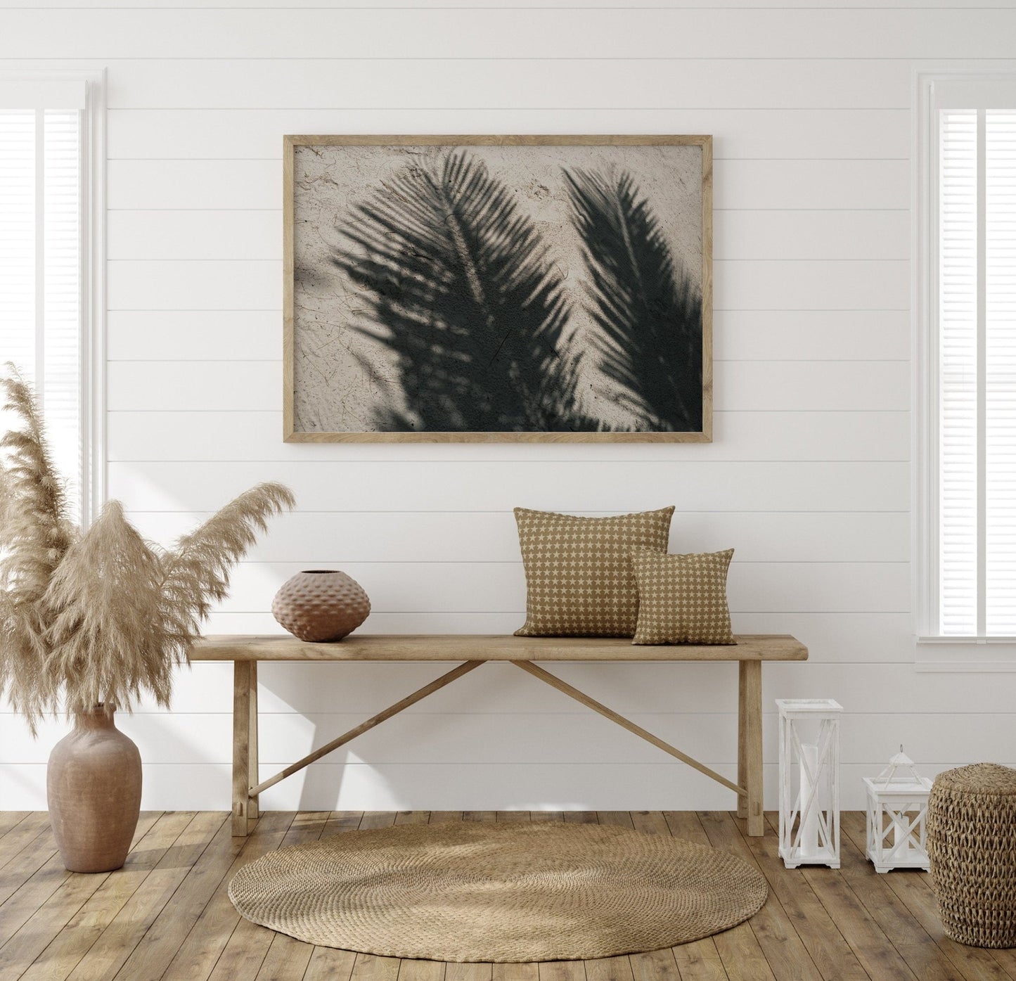 Minimalist room with a wooden bench, cushions, pampas grass, a round rug, and Palm Shade art on white shiplap walls.
