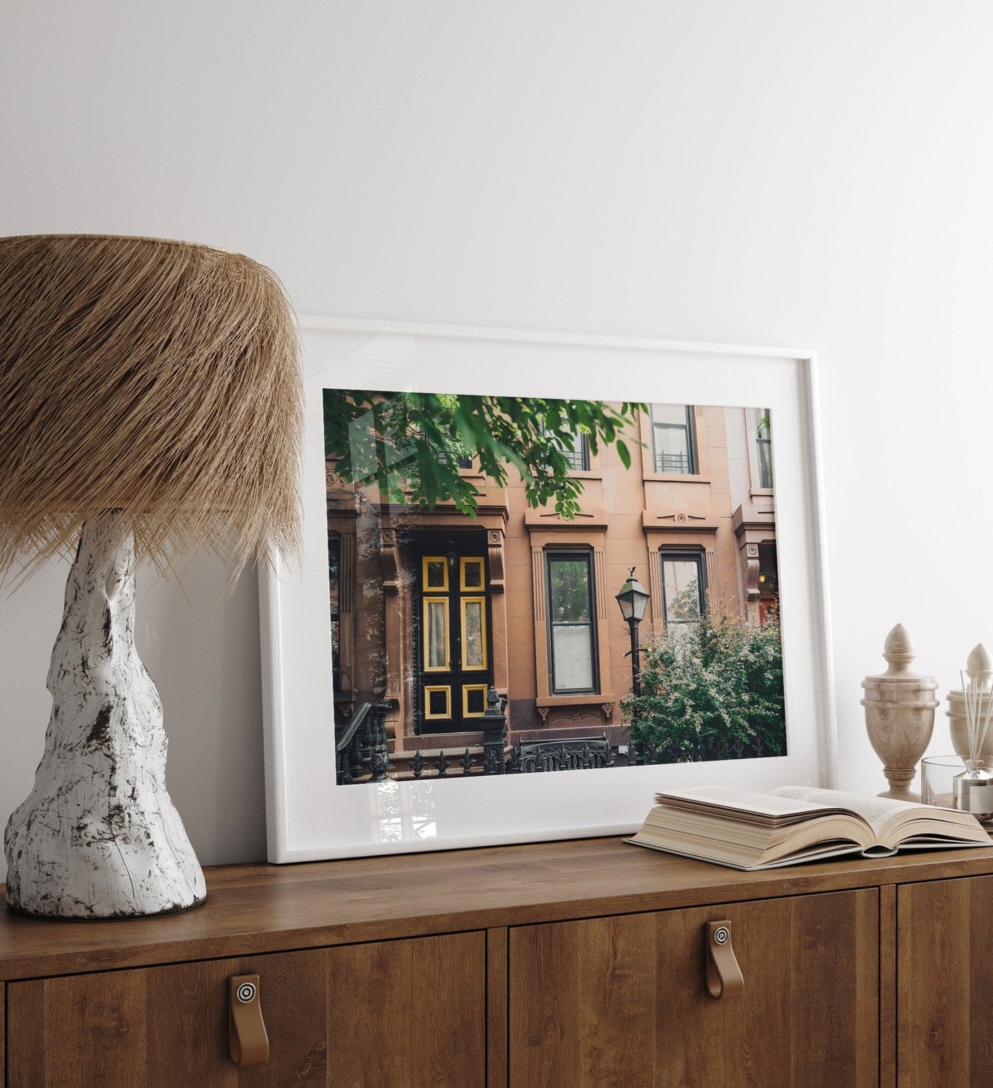 Framed photo Park Slope on a wooden cabinet beside a unique lamp, an open book, and decorative items.