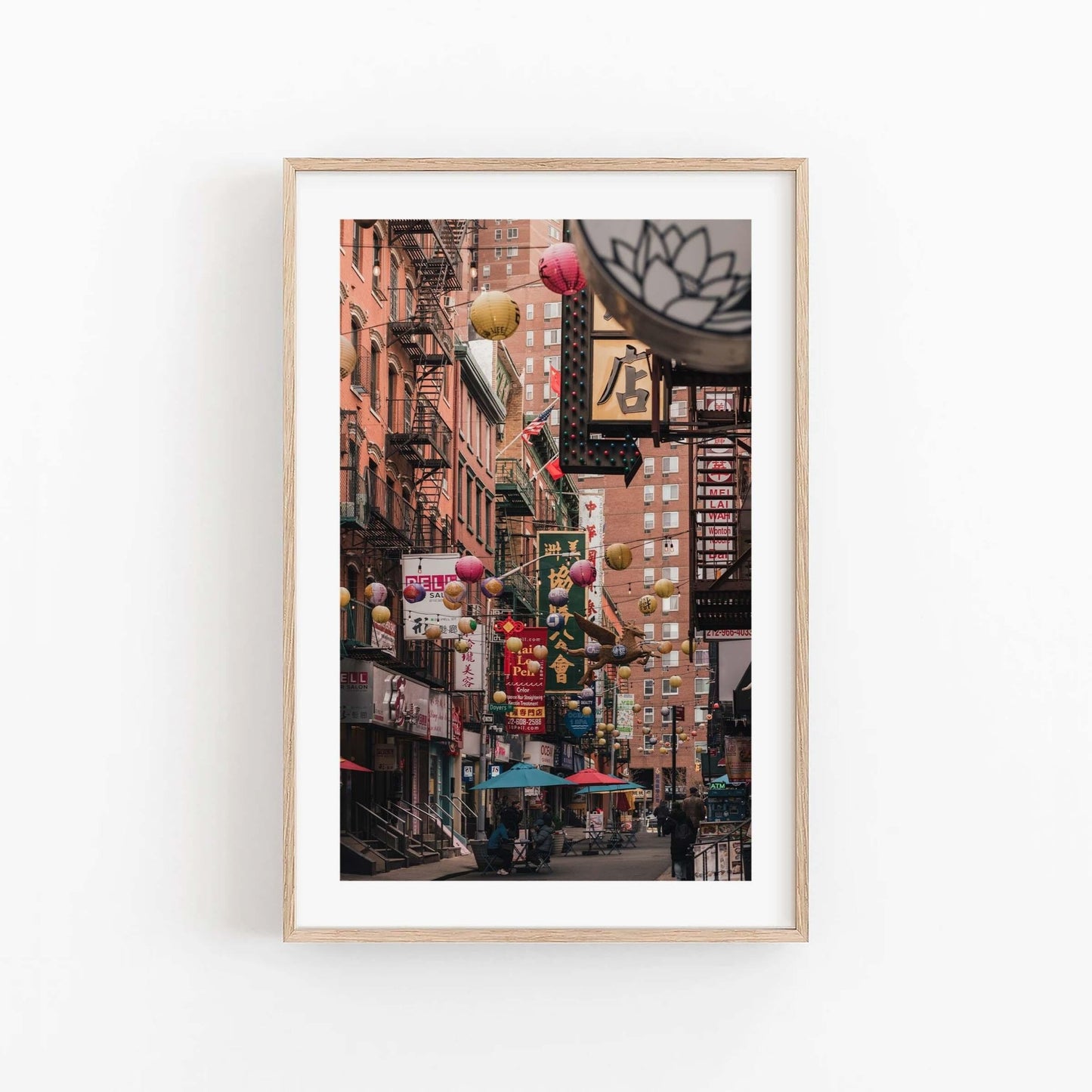 Framed Pell Street scene with colorful lanterns and signs, displayed on a white wall.