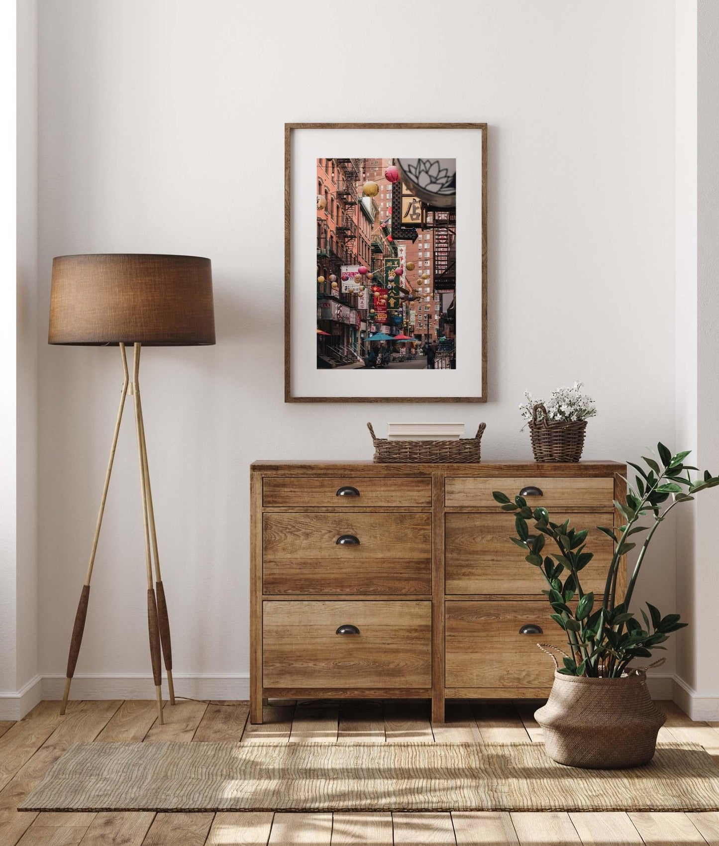Cozy room with a wooden dresser, floor lamp, plant, and the Pell Street artwork of a vibrant street scene on the wall.
