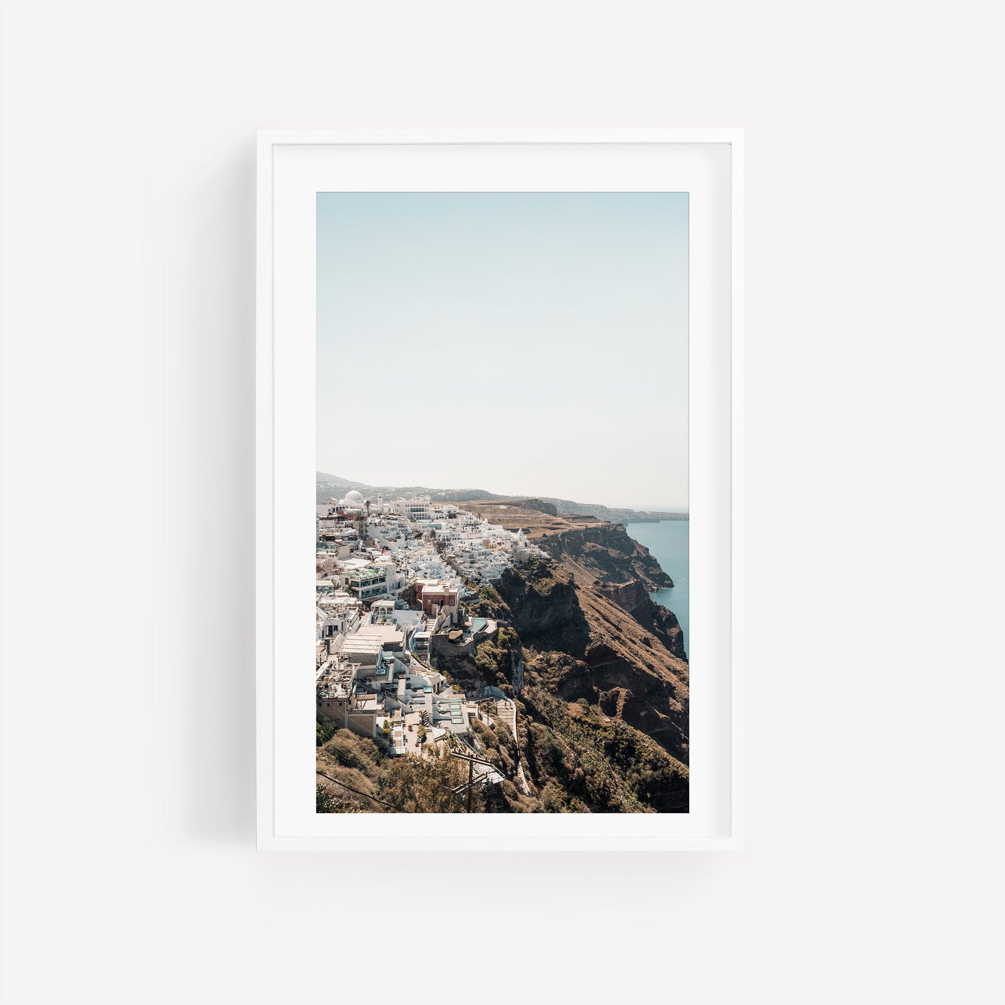 Perched framed photo of white buildings on a cliffside above the sea under a clear sky.
