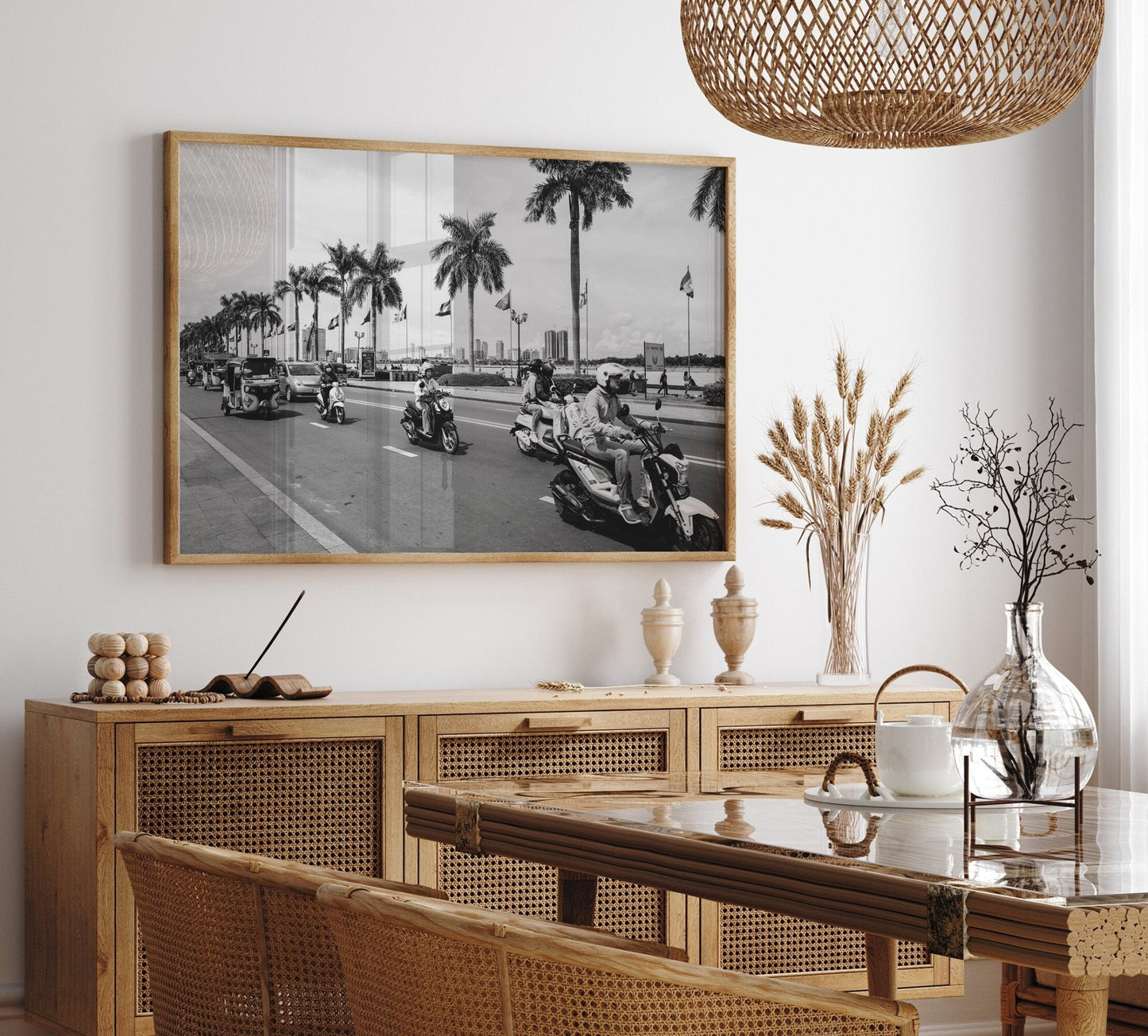 A stylish dining room with a wooden table, wicker chairs, and the framed Phnom Penh Black and White photo on the wall.
