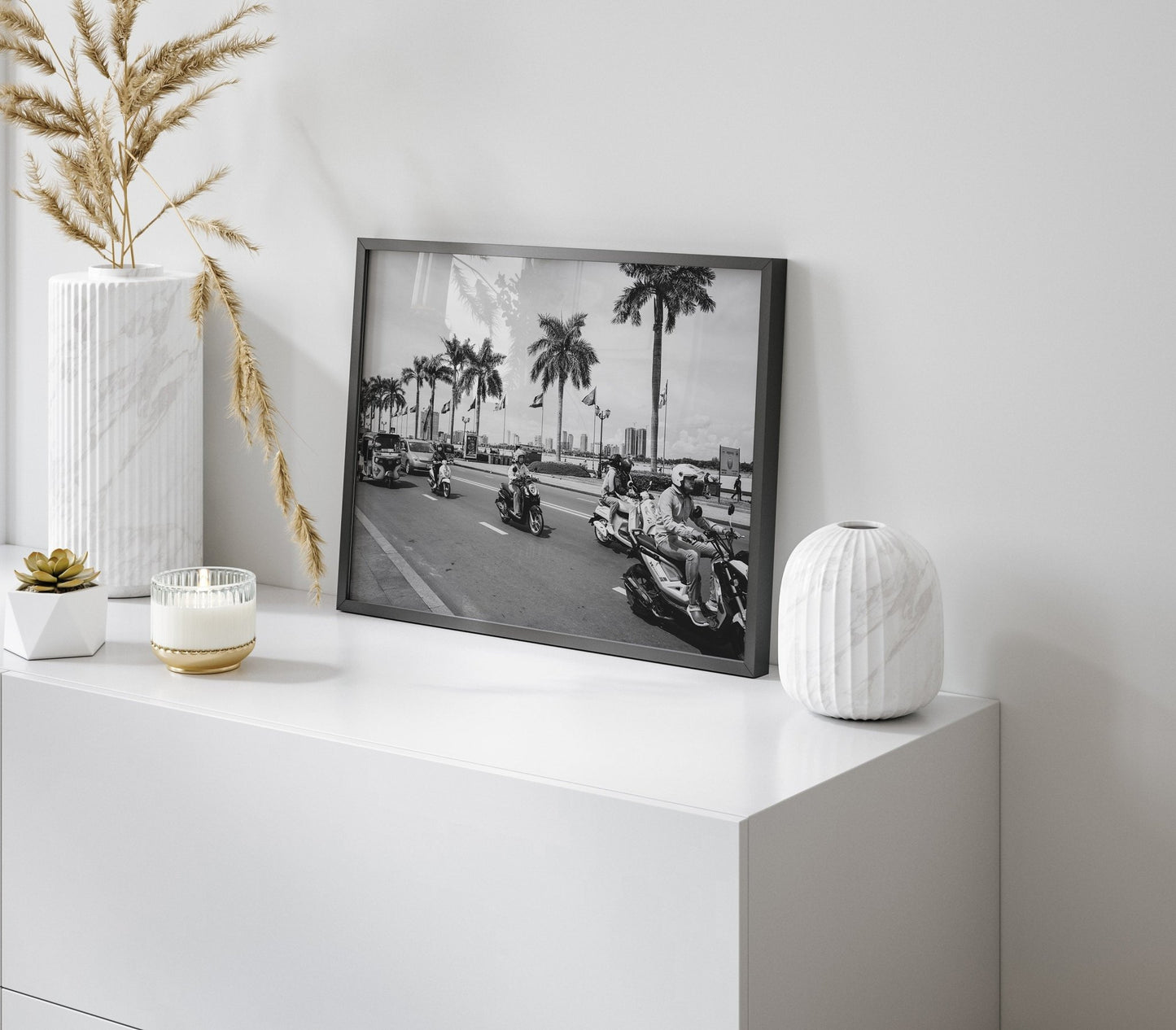 The Phnom Penh Black and White photo of a palm-lined street is displayed on a white cabinet with decorative vases.