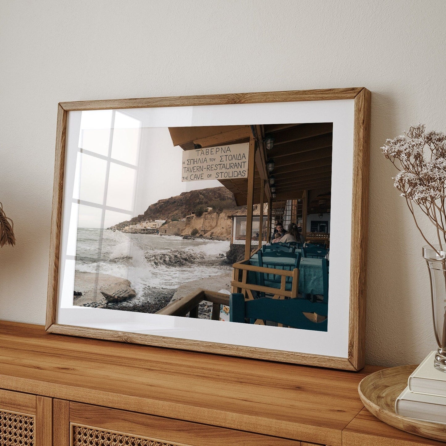 Framed Rainy Day photo on wooden dresser with a seaside taverna, waves, and cliffs in the background.