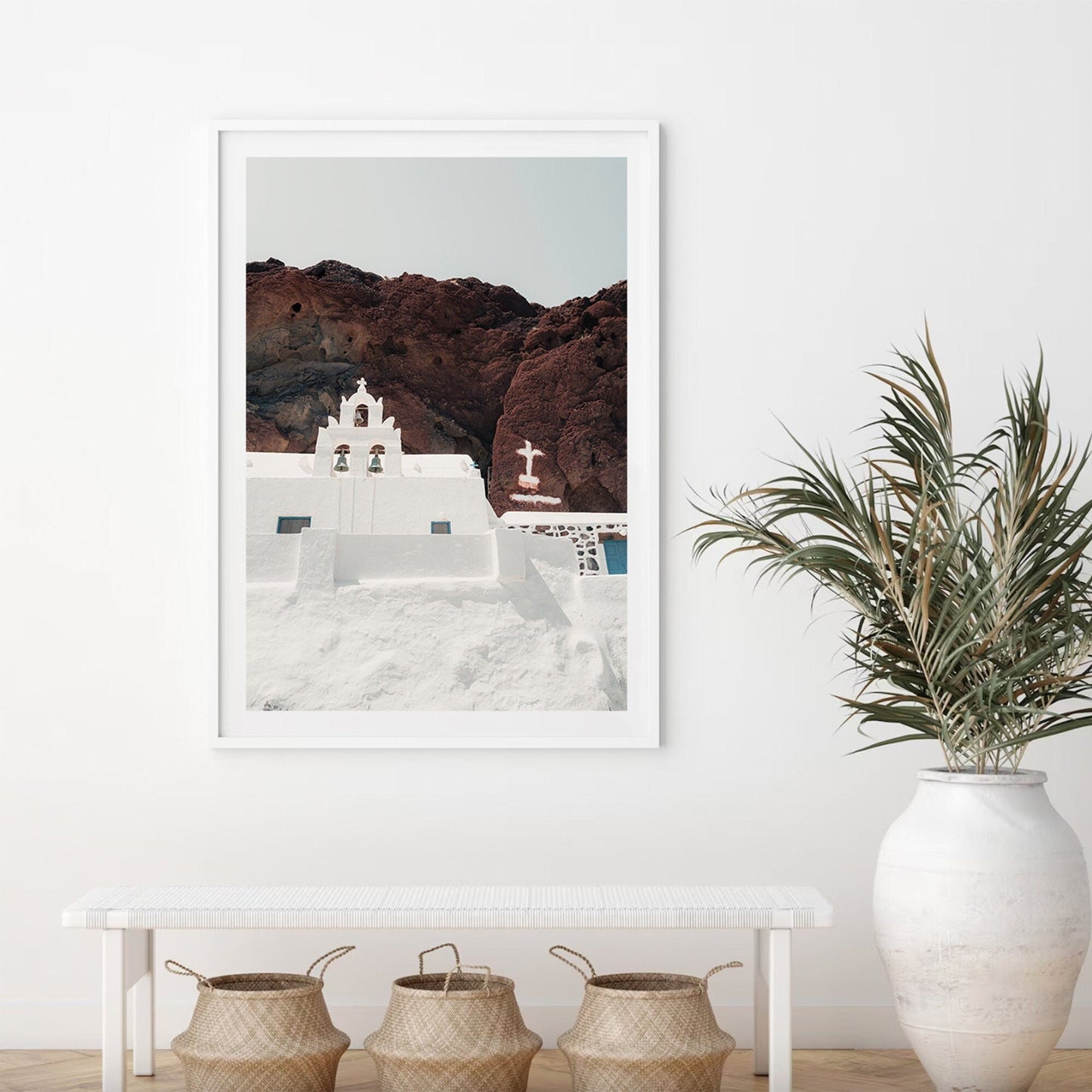 Framed Red Beach Church photo on a rocky hill above a bench with baskets and a large potted plant.