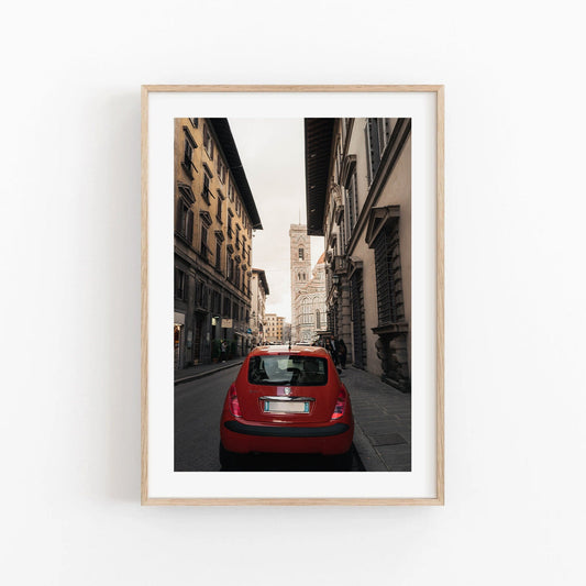 Framed photo titled Red Car shows a narrow street with historic buildings and a distant tower.