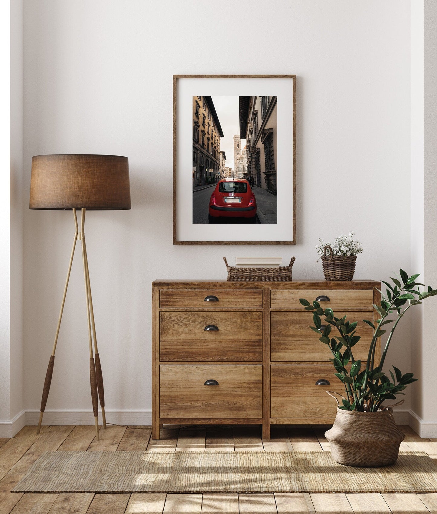 A cozy room featuring a wooden dresser, standing lamp, framed photo, potted plant, and a red car.