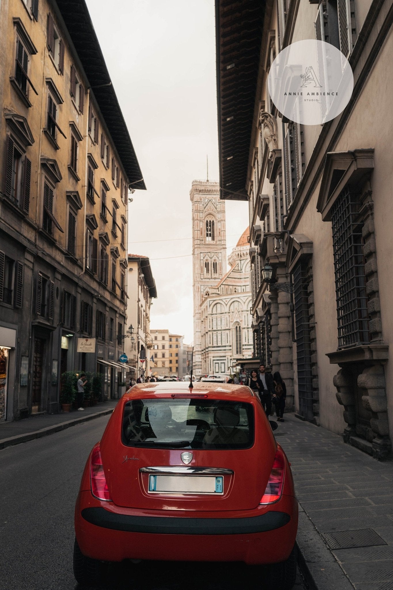 Red Car navigating a narrow street with a historic building in the background.