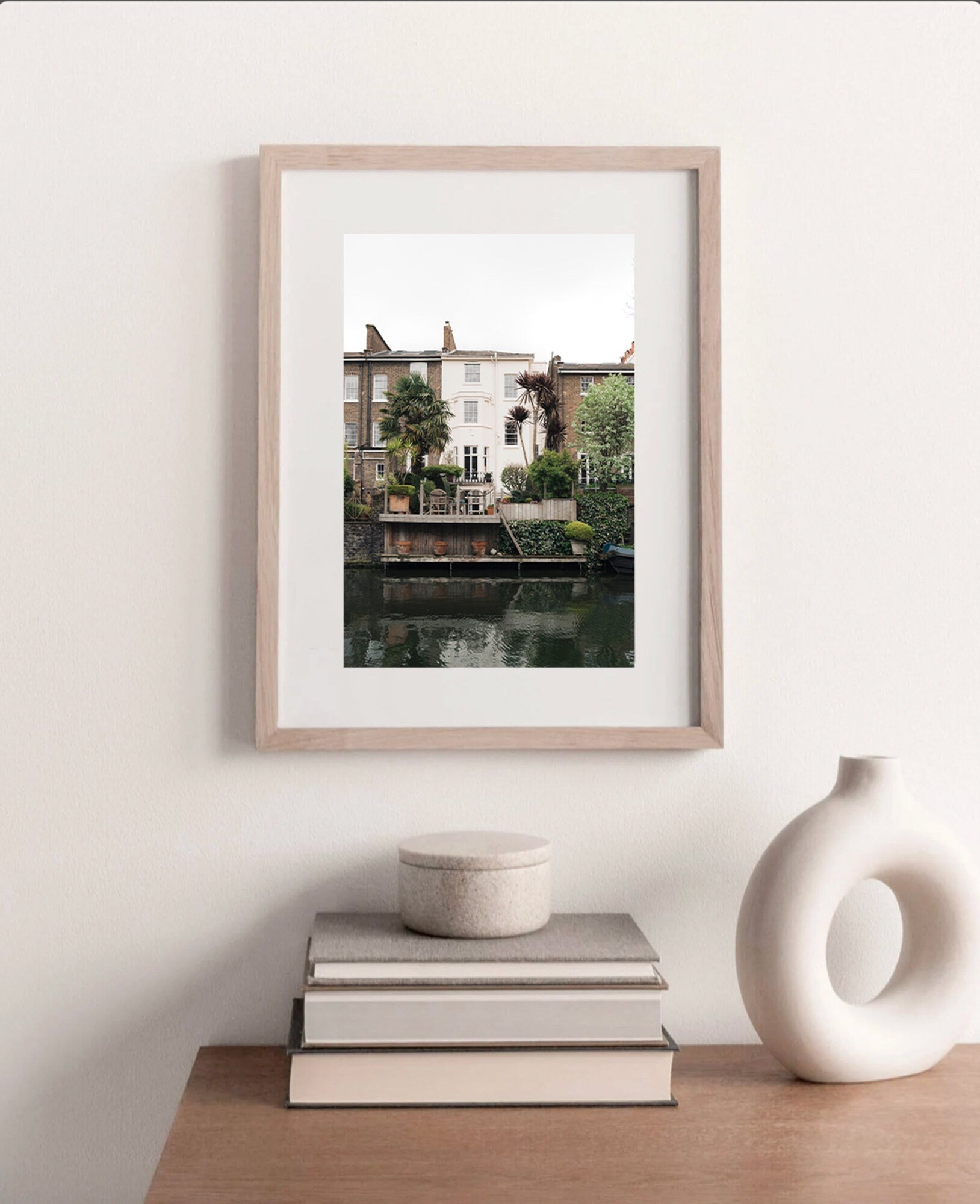Regents Canal photo framed on a white wall above a wooden table with books and decor.