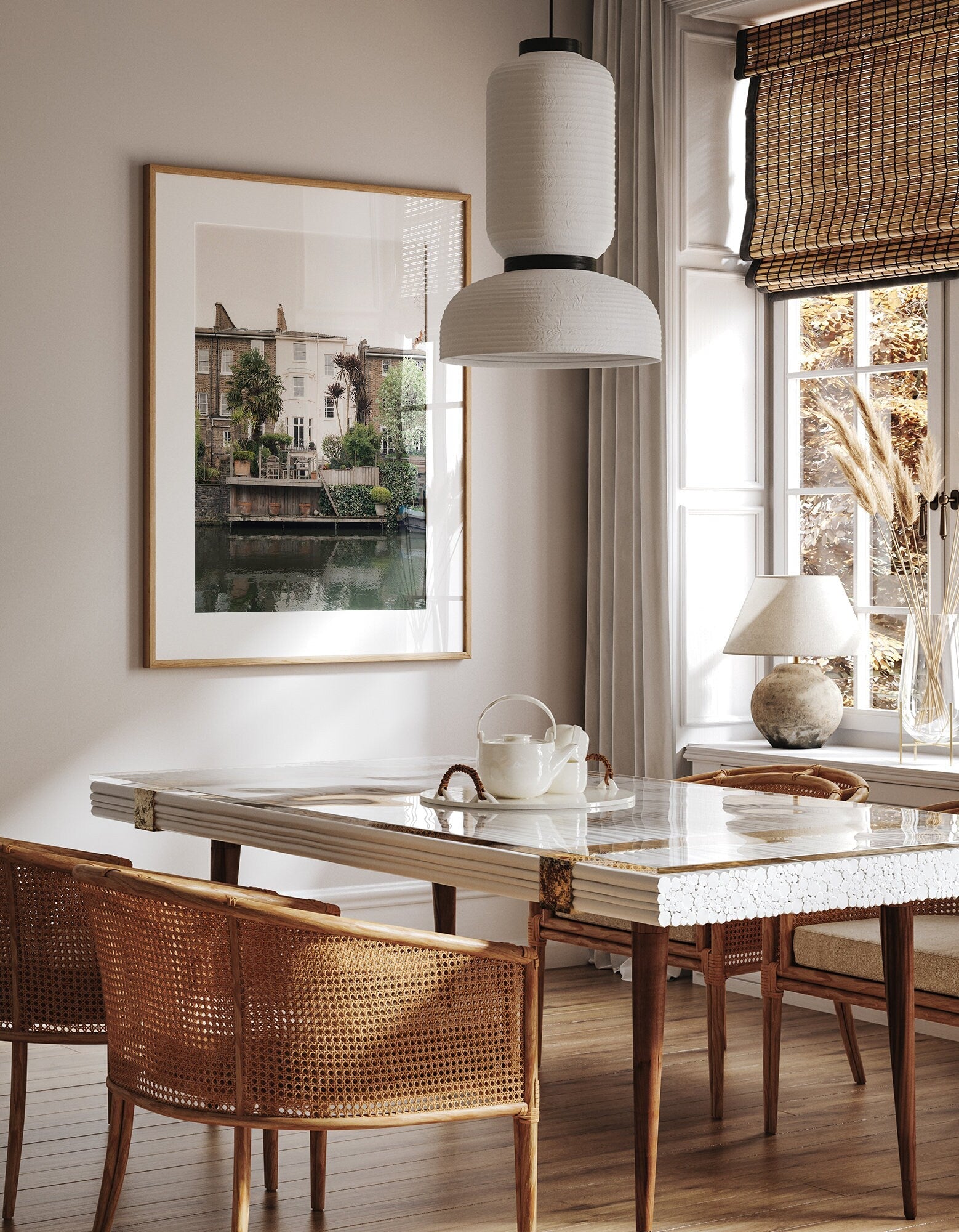 A cozy dining room with Regents Canal wicker chairs, a marble table, pendant light, and framed wall art by a window.