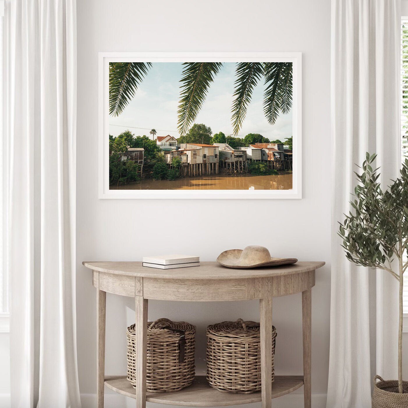 The River Homes photo is framed on a wall above a wooden table with baskets beneath and a plant beside it.
