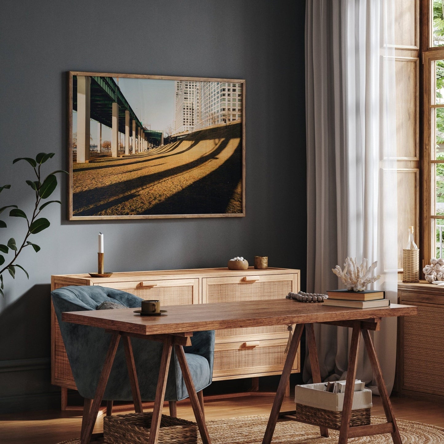 A cozy room with a wooden desk, chair, dresser, large window, and a framed Riverside photo of a bridge on the wall.