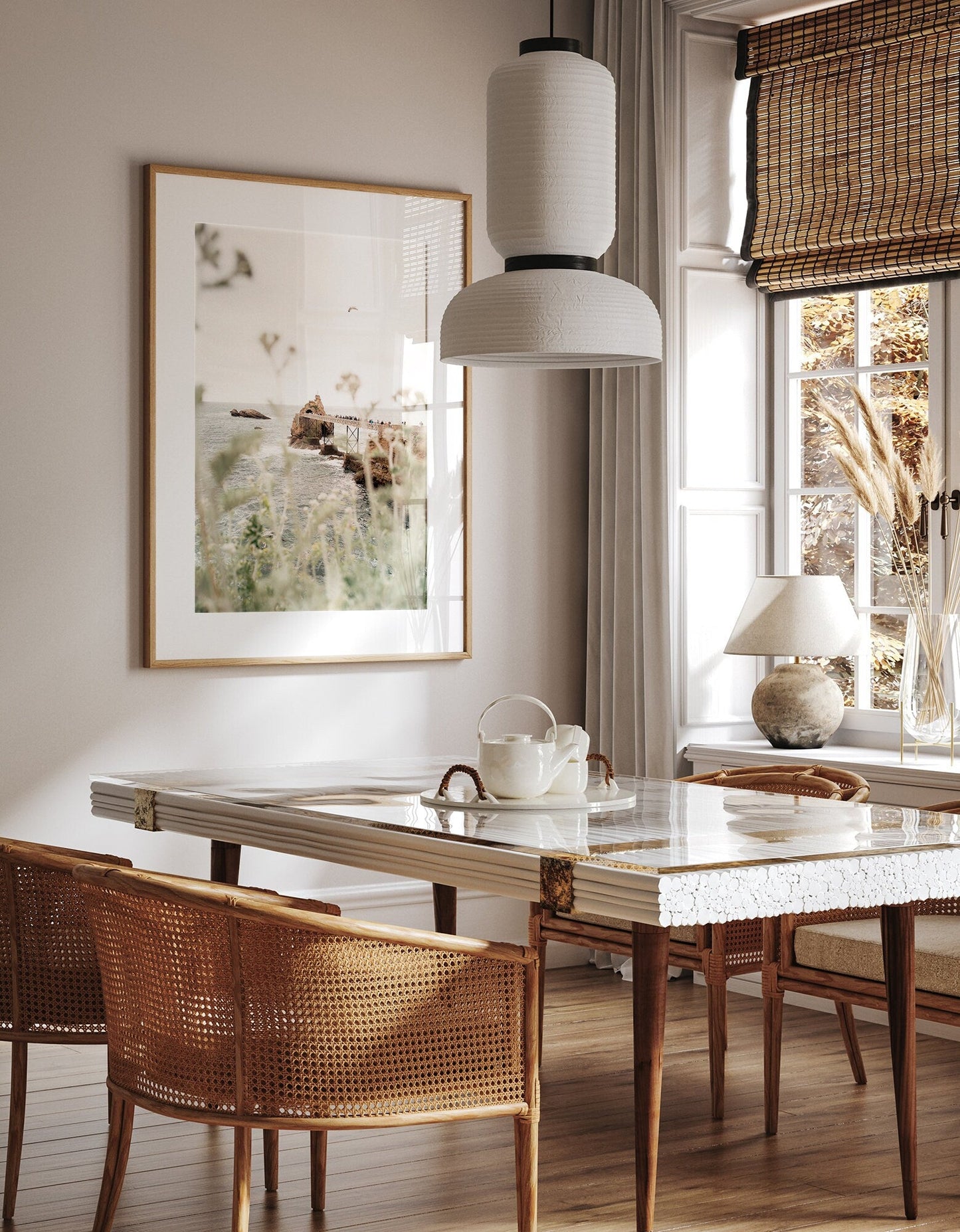 A cozy dining room with a Roche de le Vierge table, wicker chairs, pendant lamp, bamboo blinds, and nature artwork.
